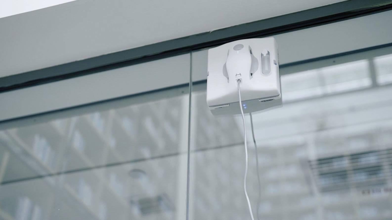 Un robot aspirateur de vitres est fixé à une grande surface vitrée et est alimenté par un câble pendant qu'il travaille.