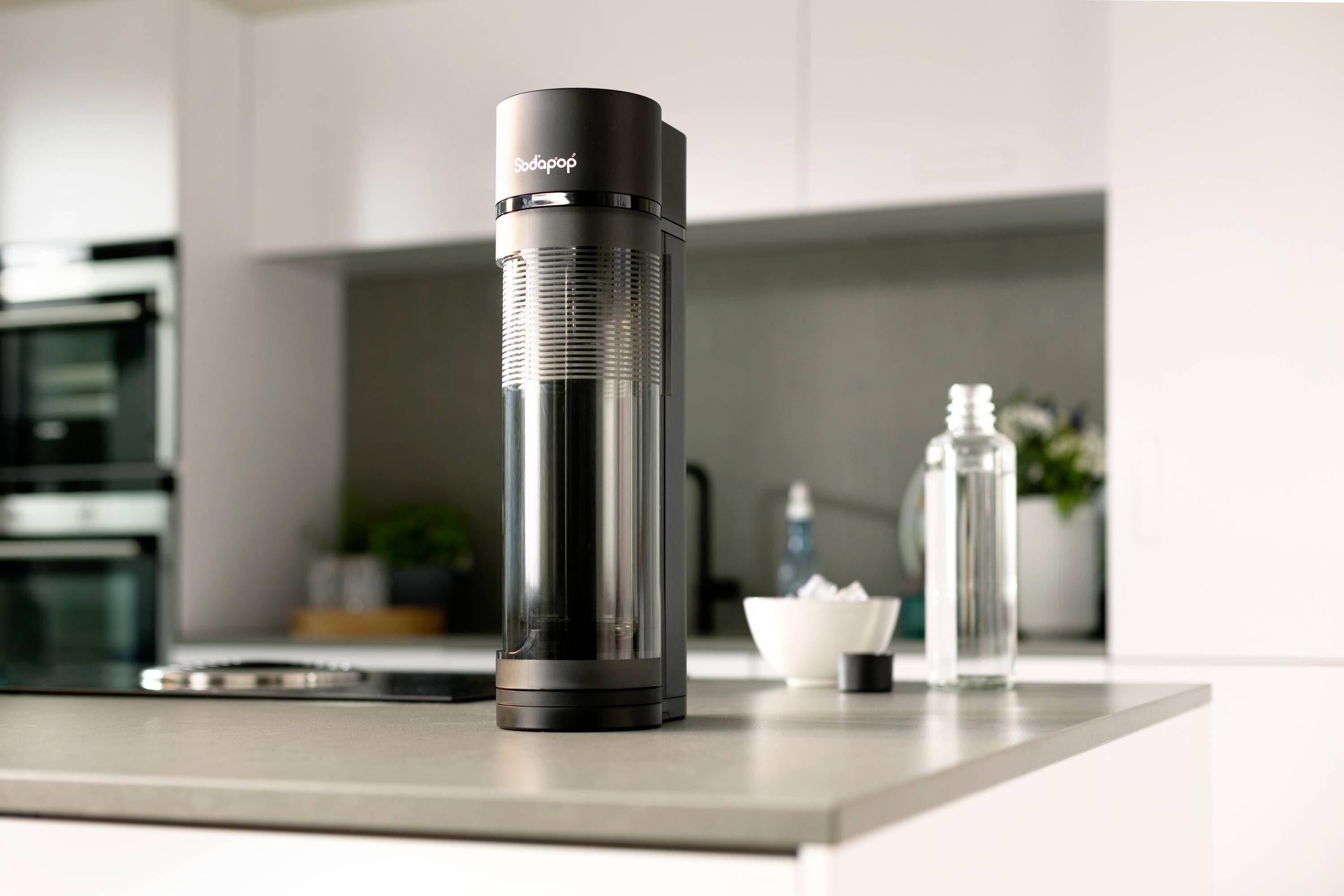 Machine à gazéifier l'eau SodaStream sur un plan de travail de cuisine. Des bouteilles et un bol sont visibles en arrière-plan.