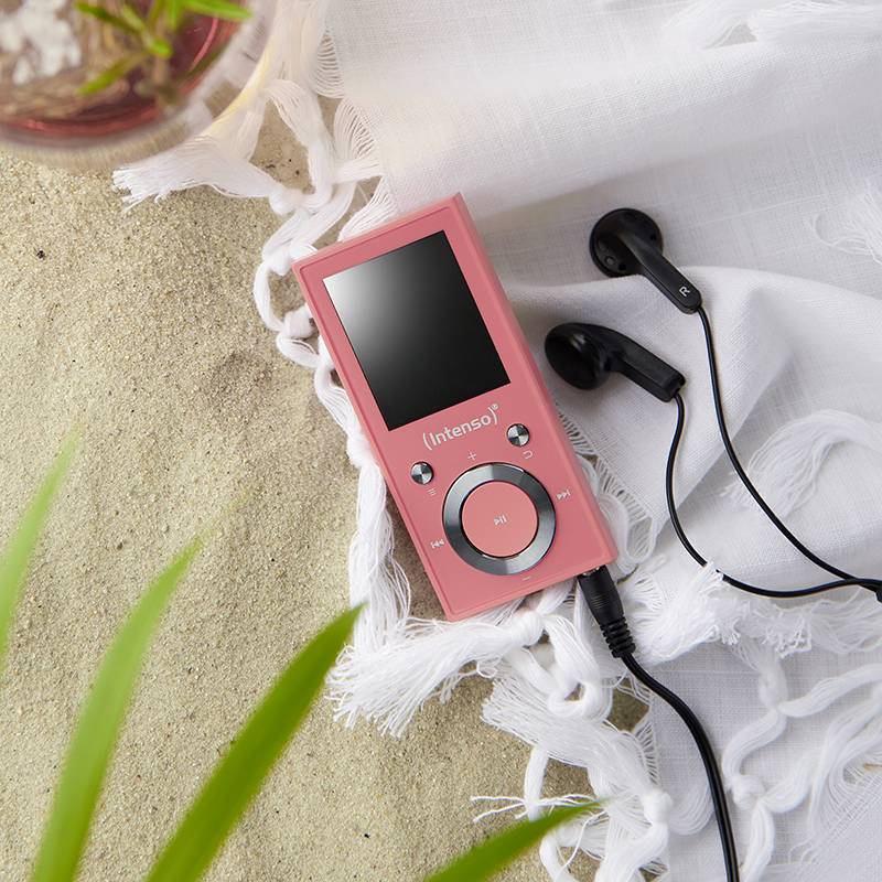 Un lecteur de musique rose avec des écouteurs est posé sur un tissu blanc, à côté d'une boisson et de plantes en arrière-plan.