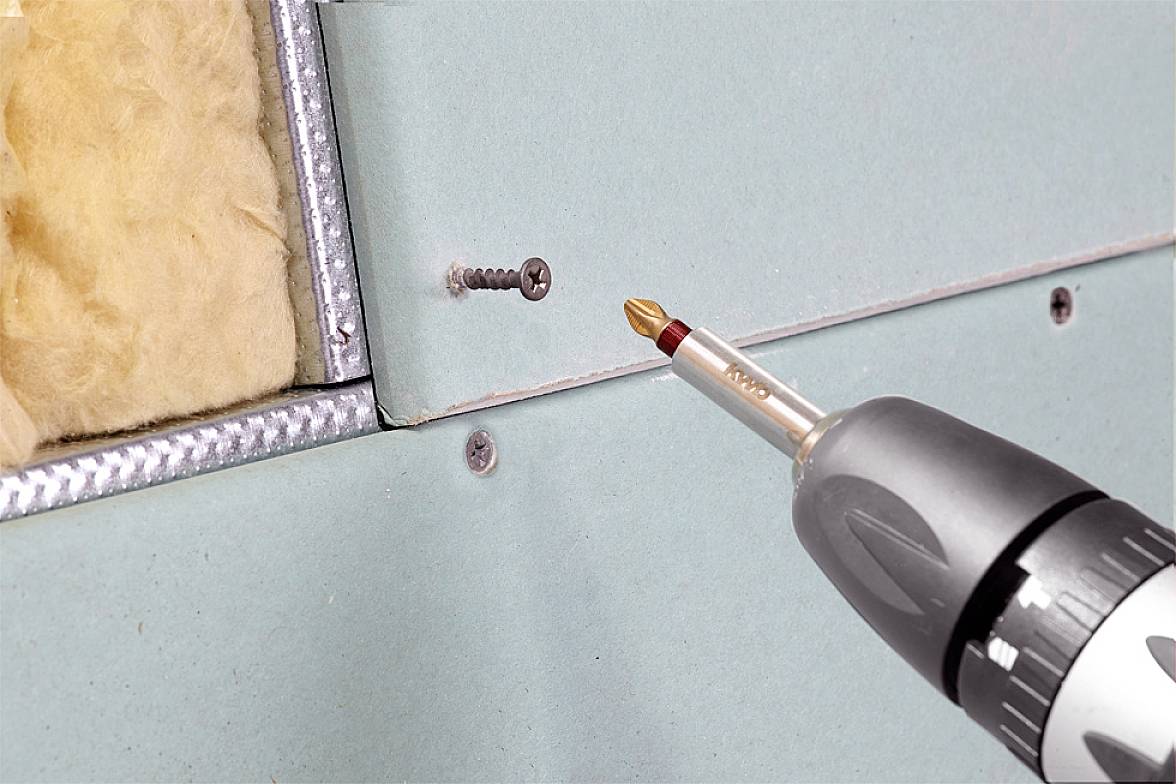 Un tournevis sans fil avec un embout de vissage enfonce une vis dans une plaque murale remplie de matériau isolant.