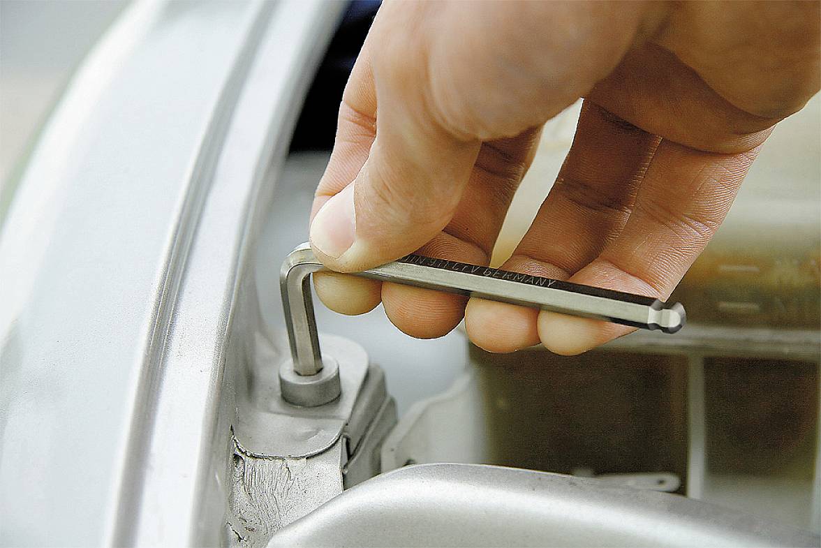 'Gros plan d'une main utilisant une clé hexagonale pour visser une vis sur un cadre métallique argenté.'