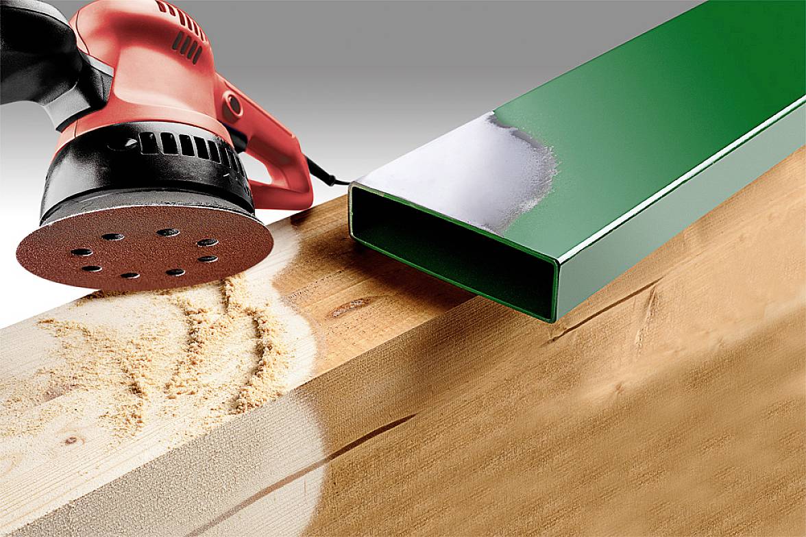 Un ponçeur excentrique rouge lisse une surface en bois. À côté, un boîtier métallique vert sert de comparaison pour les surfaces lisses.