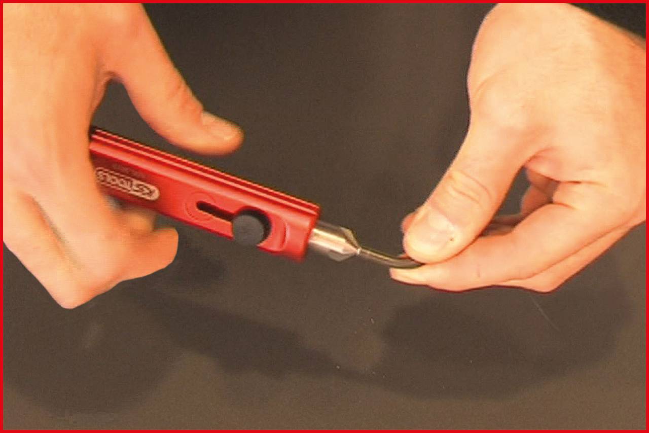 Une personne tient un outil de précision rouge avec une lame à la main, prête à effectuer des travaux de coupe précis.