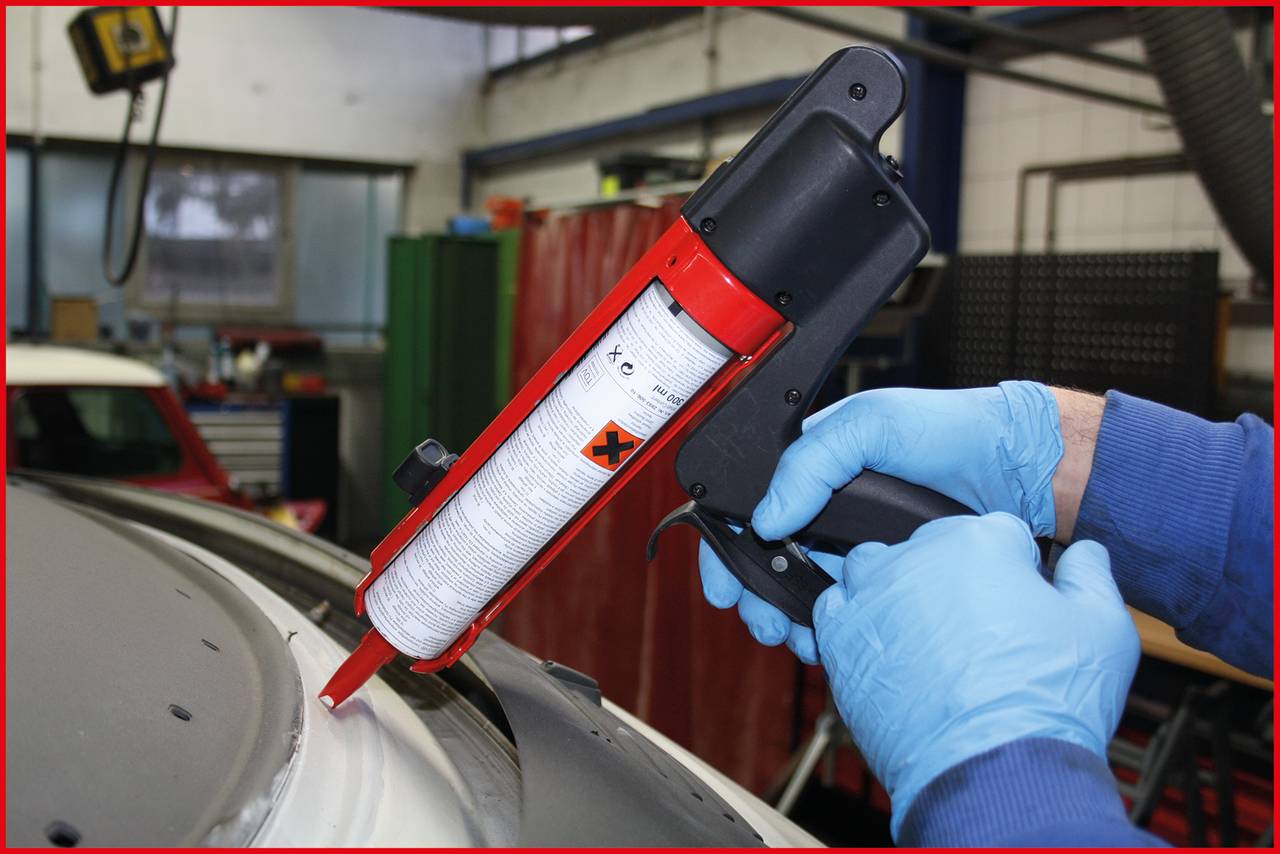 Une personne portant des gants bleus applique un mastic sur le toit d'une voiture afin de sceller soigneusement une jointure.