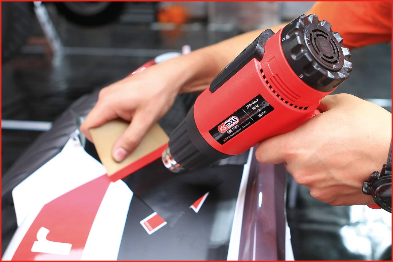 Une personne utilise un pistolet à air chaud pour appliquer un film adhésif sur une surface.