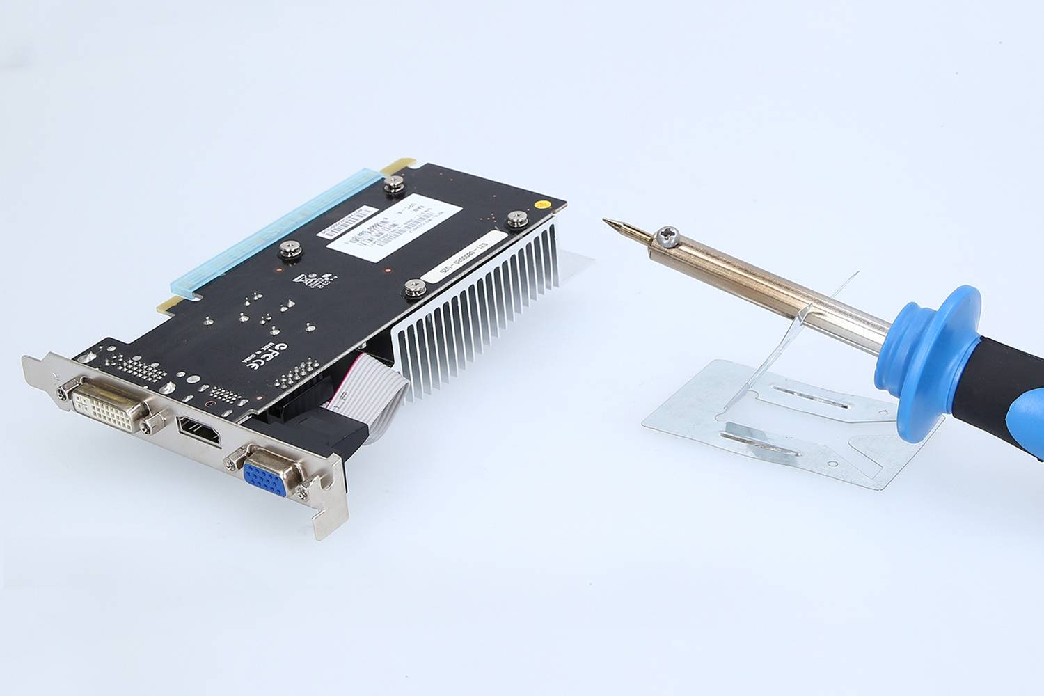 Carte graphique et fer à souder sur une surface. La carte graphique présente différents ports, dont DVI et VGA.