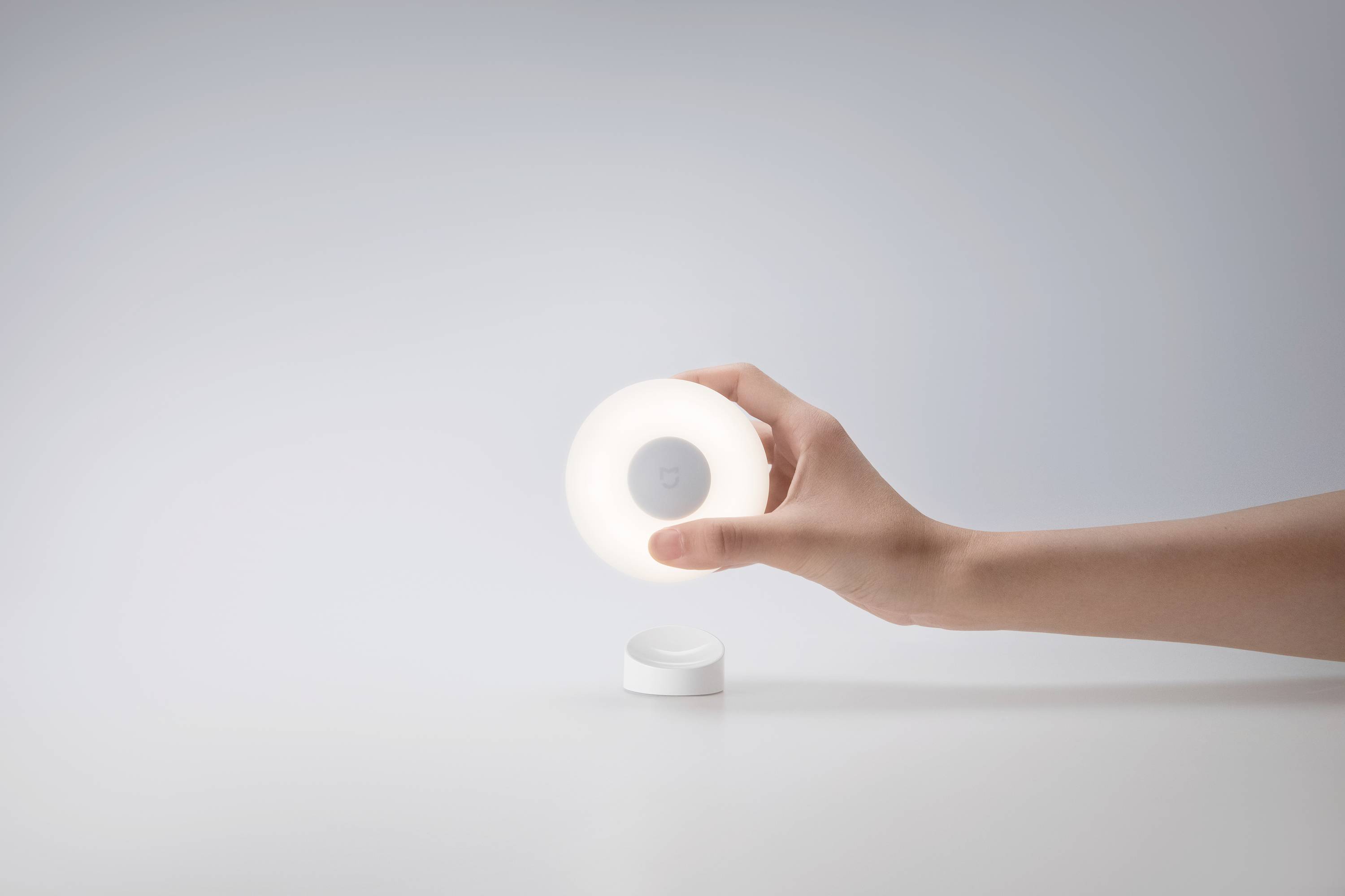 Une main tient une veilleuse ronde et lumineuse au-dessus d'un fond blanc.