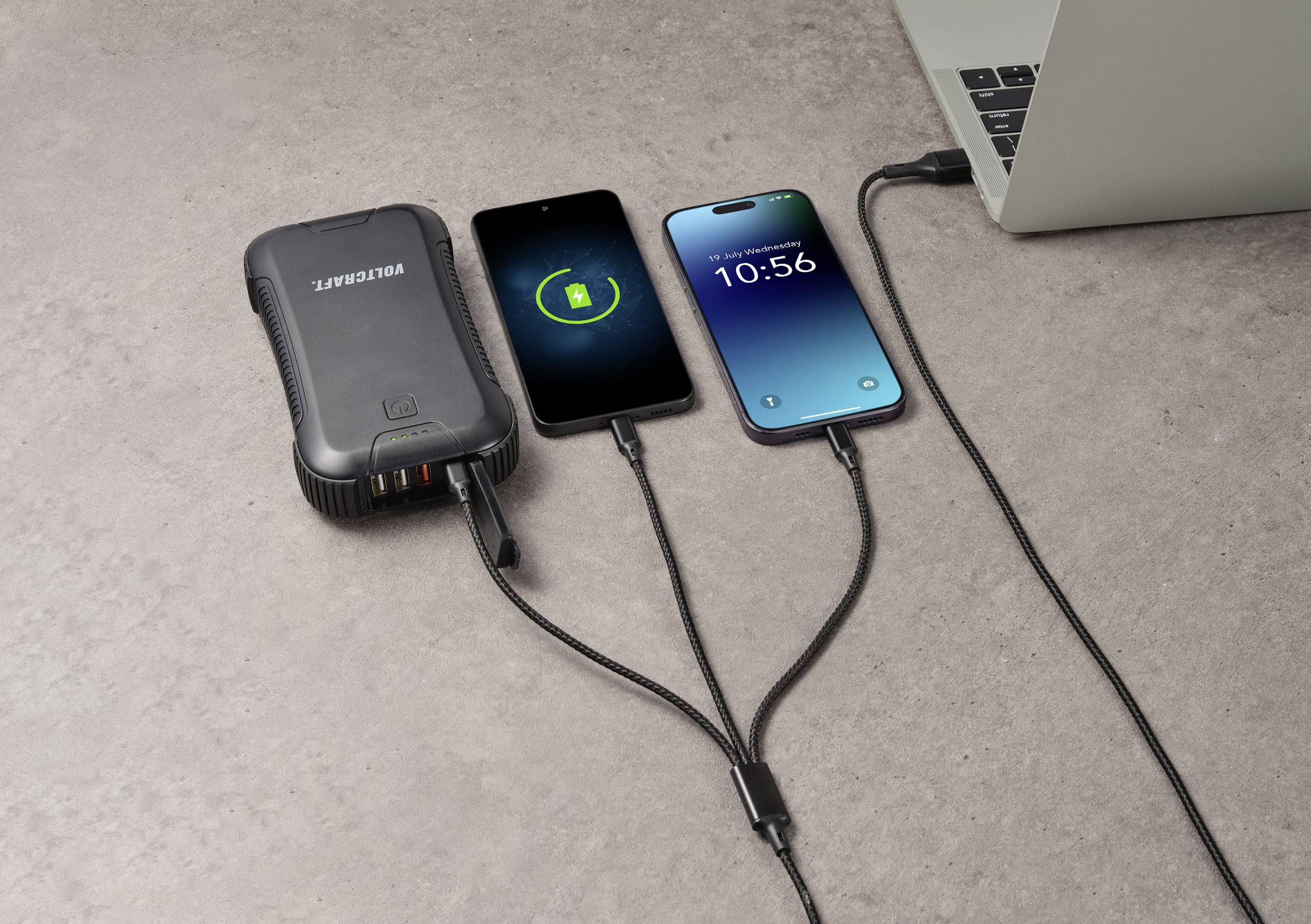 Quatre appareils sont connectés sur une surface en béton : Une batterie externe, deux smartphones en charge et un ordinateur portable.