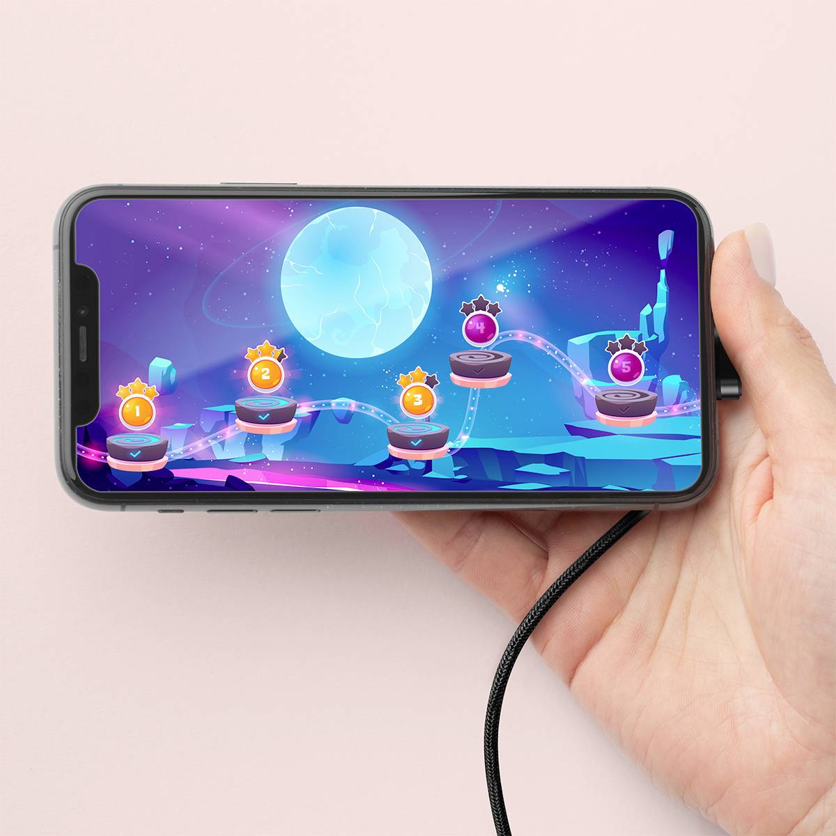 Une main tient un smartphone dont l'écran affiche un jeu vidéo avec des niveaux composés de boules lumineuses sur un fond d'univers bleu parsemé d'étoiles.