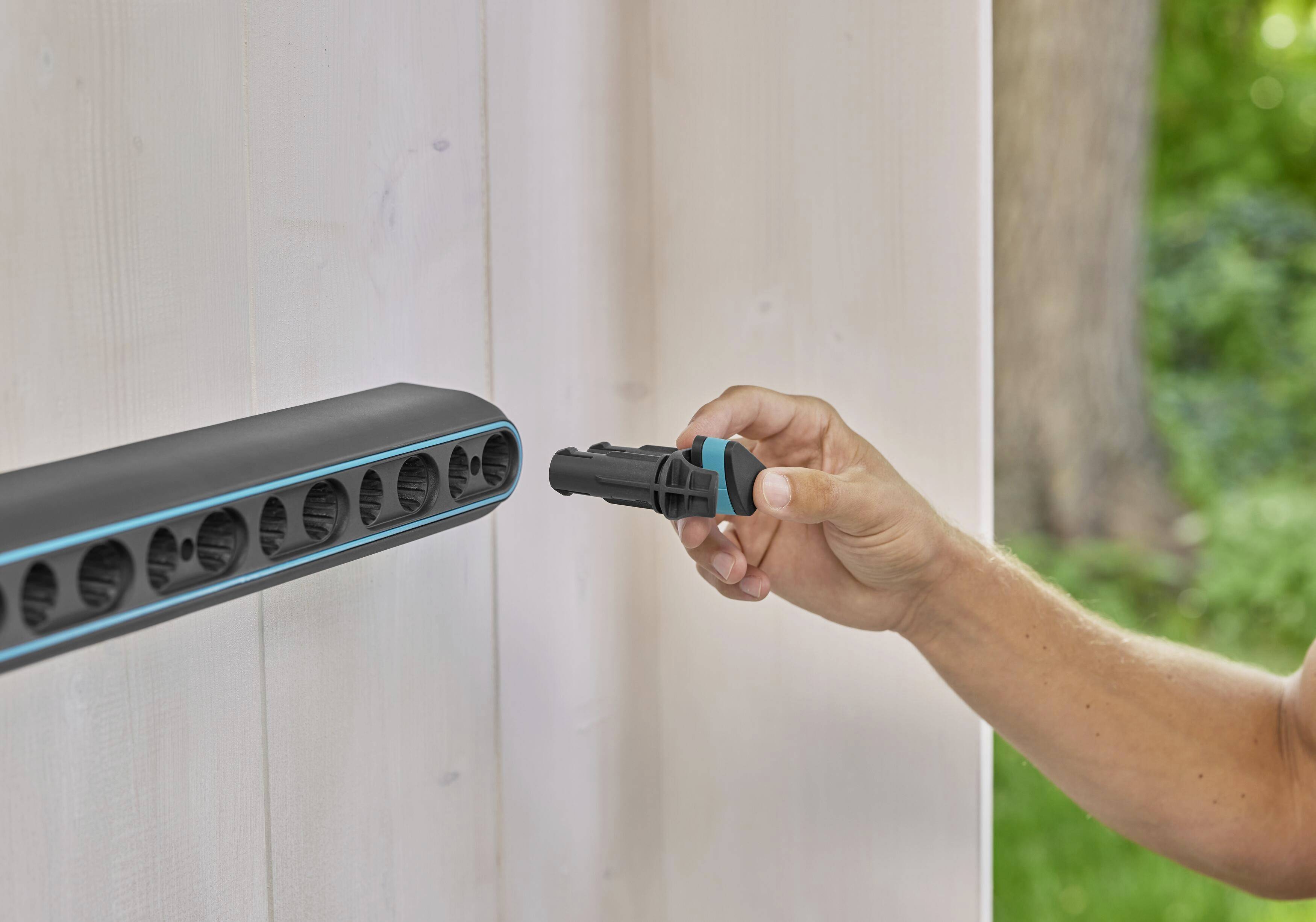 Une personne branche une fiche noire sur une barre horizontale fixée sur un mur extérieur.