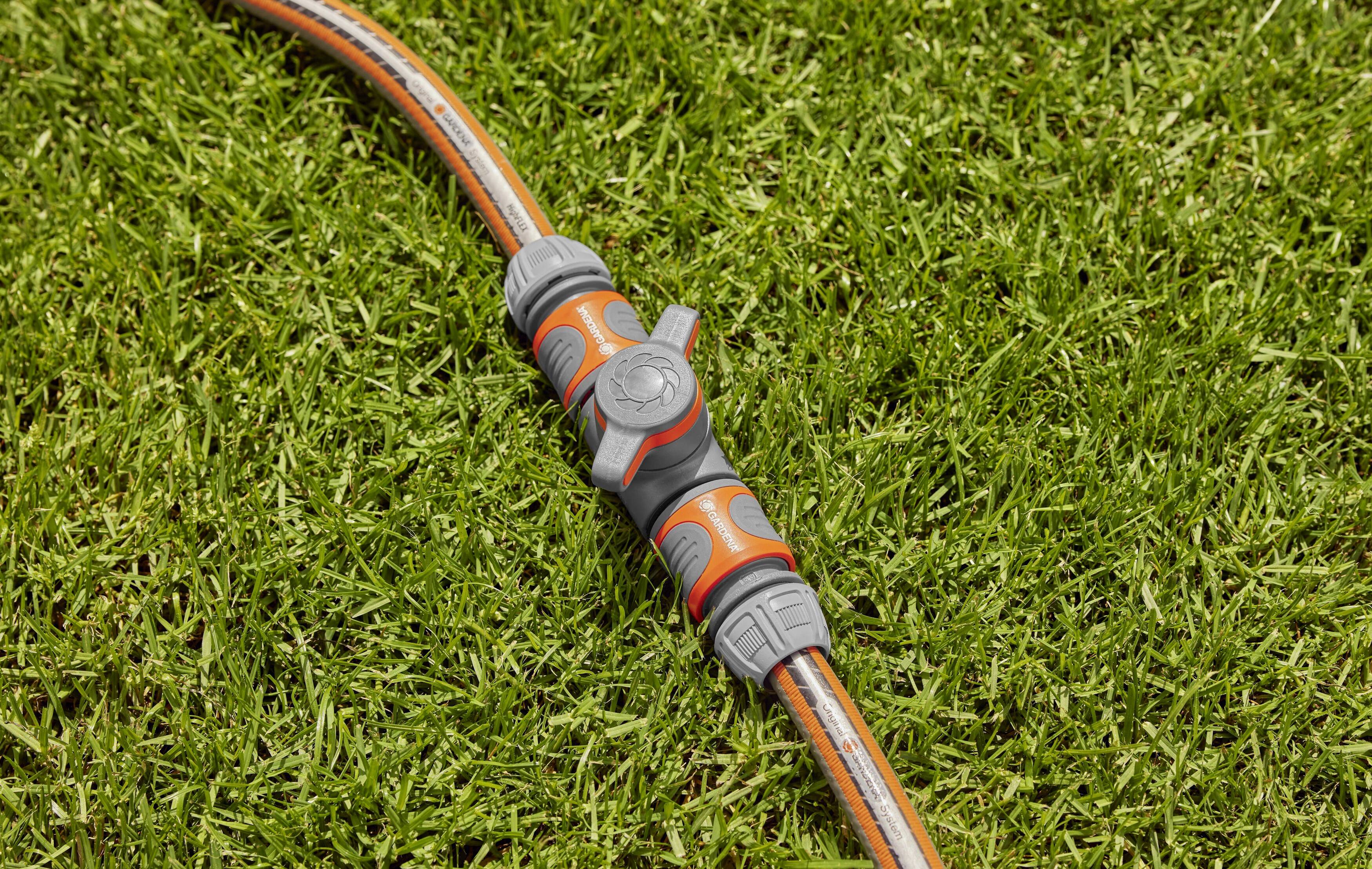 Un tuyau d'arrosage avec un raccord est posé sur de l'herbe verte. Le raccord est gris et orange et sert à contrôler l'eau.