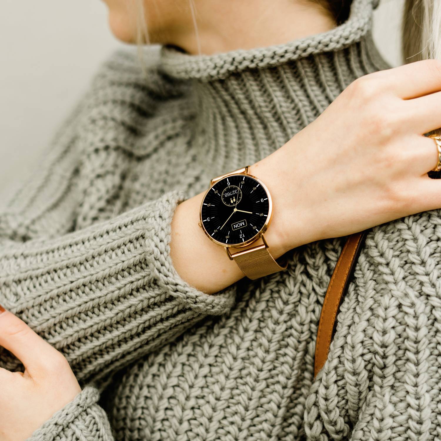 Une personne porte un pull en tricot gris et une montre-bracelet analogique élégante avec un bracelet marron.