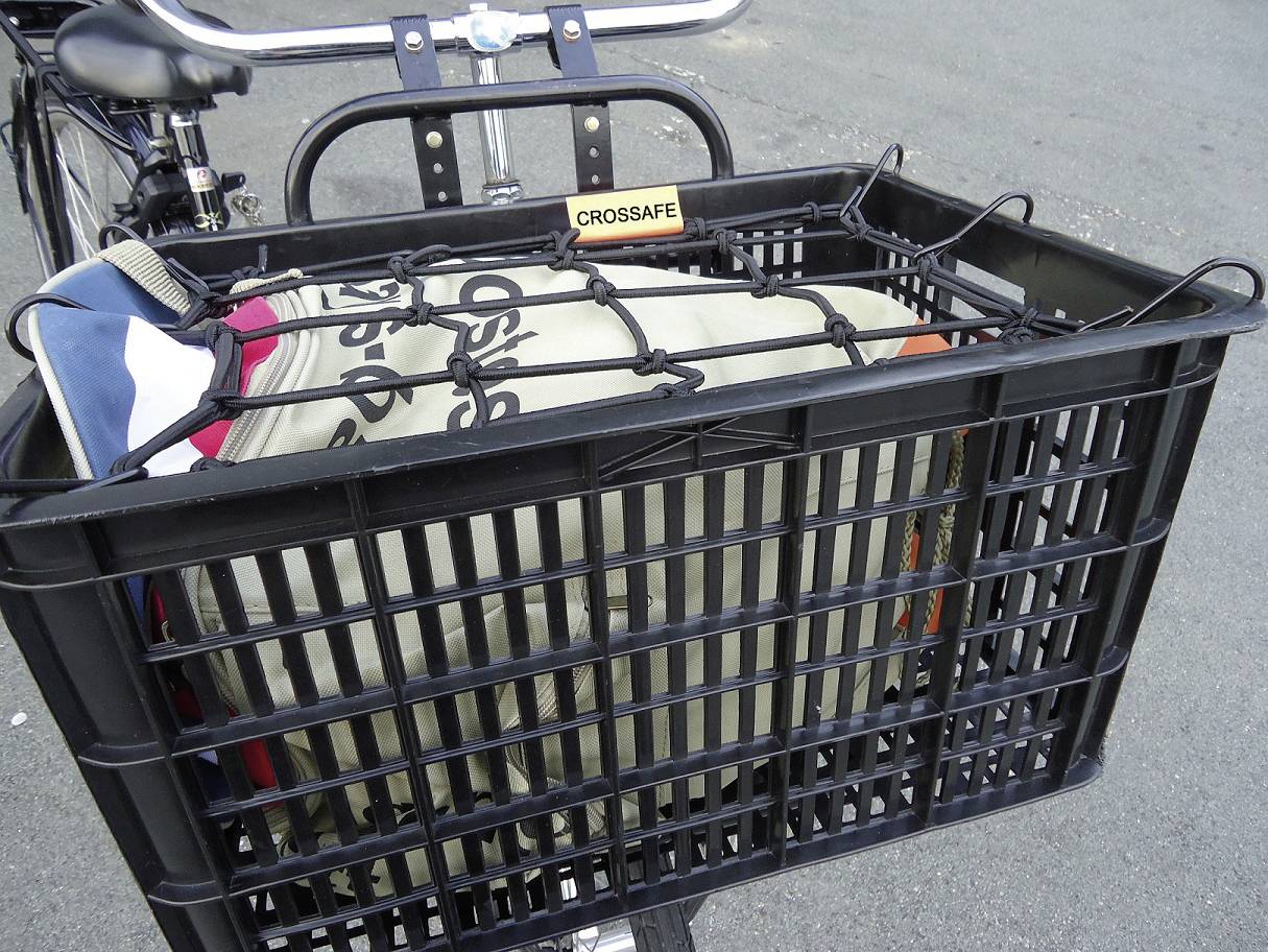 Un panier de vélo contenant un article de bagages attaché, enveloppé d'un filet noir. Le panier est fixé à l'avant du vélo.