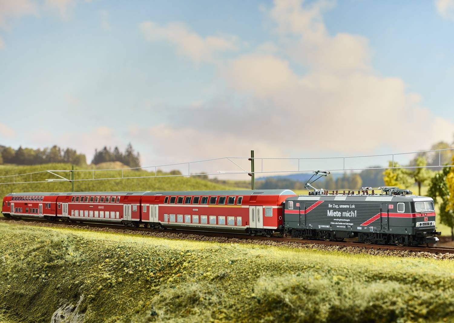 Train avec des wagons à double étage de couleur rouge circulant à travers un paysage verdoyant sous un ciel bleu.