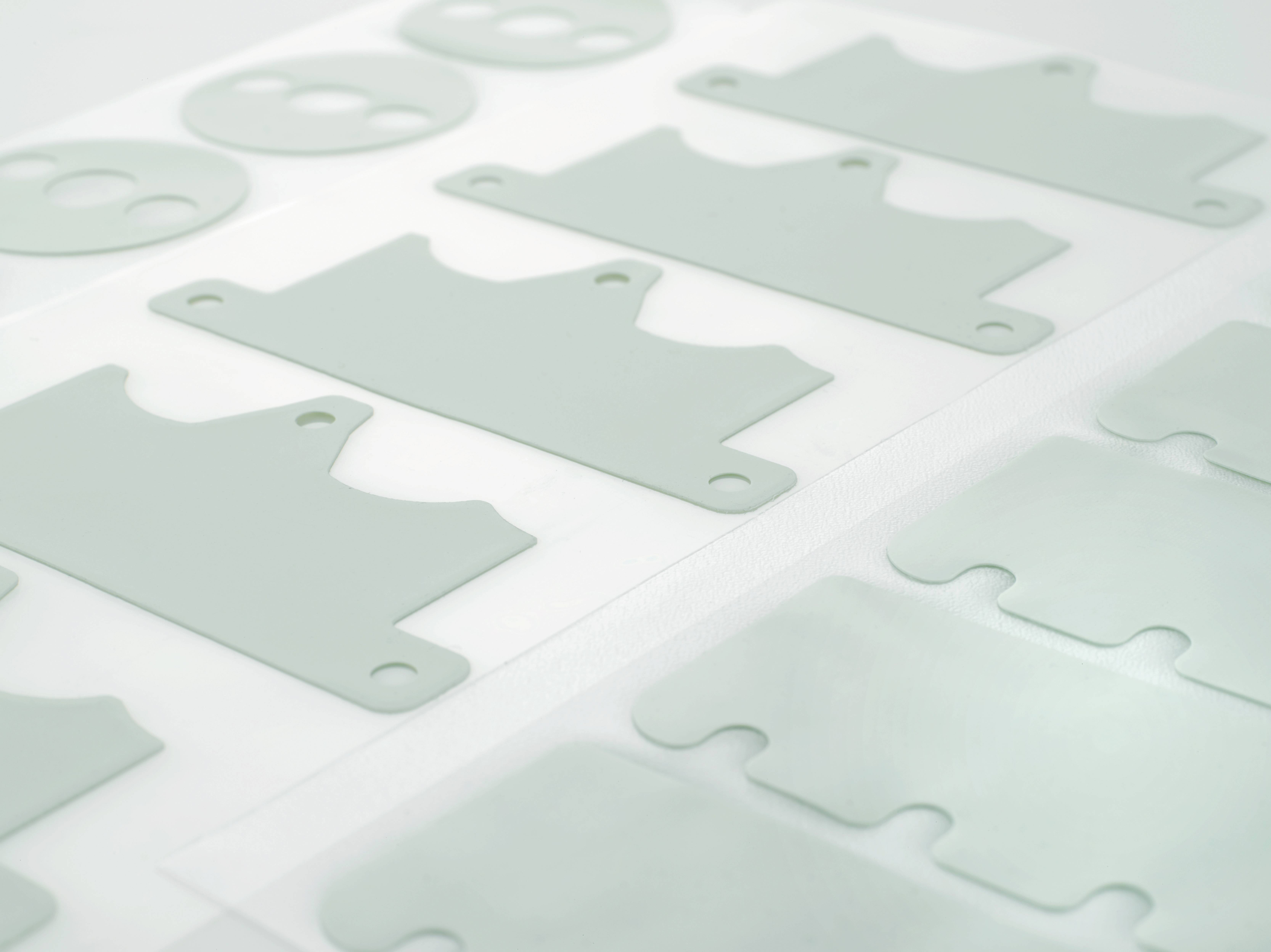 Plusieurs pièces rectangulaires en plastique gris avec des découpes circulaires sont disposées en rangée ordonnée sur des feuilles blanches.