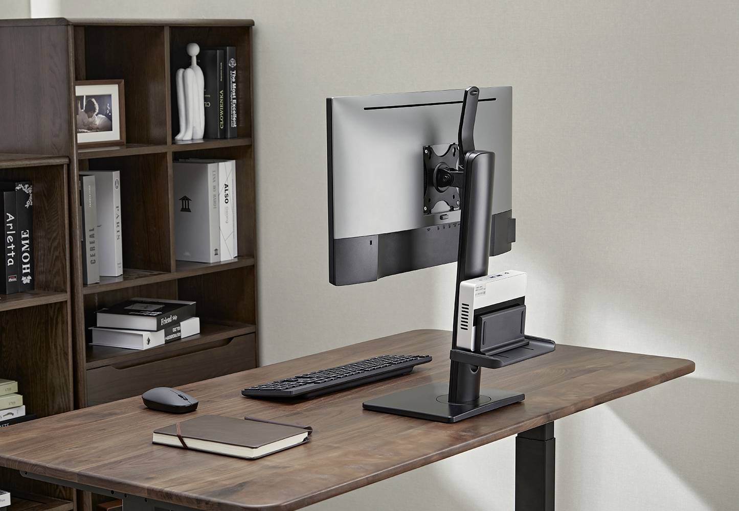 Un bureau moderne avec un écran, un clavier, une souris et un carnet de notes. À l'arrière-plan, une étagère avec des livres et des objets décoratifs.