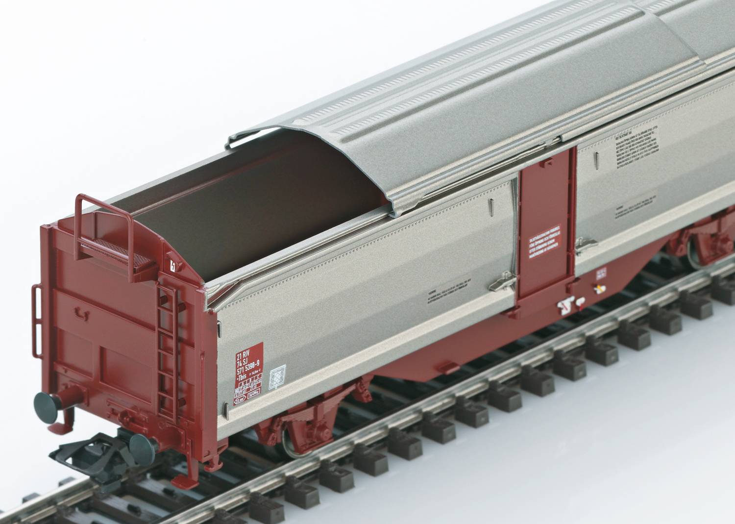 Un wagon de marchandises modèle gris et rouge, avec un toit ouvert, roulant sur des rails, adapté au transport de matériaux en vrac.