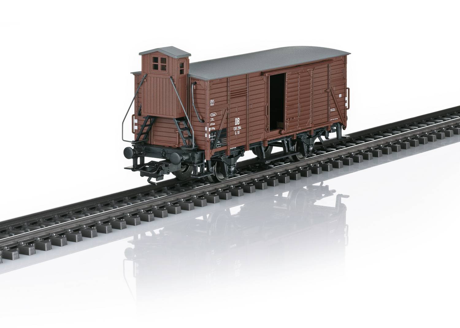 Un wagon brun est stationné sur une voie ferrée. Le wagon a une porte fermée et des roues noires.