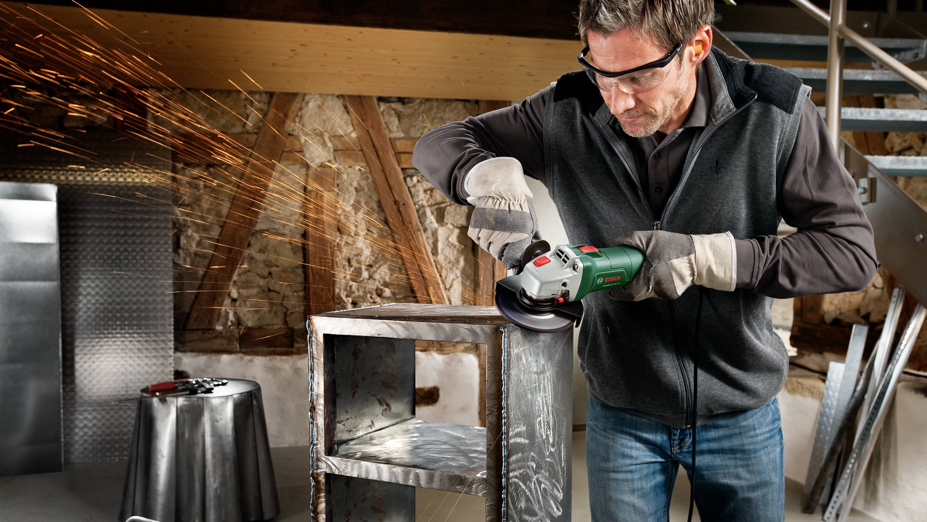 Un homme portant des lunettes de protection et des gants produit des étincelles avec une meuleuse d'angle en travaillant sur un objet métallique.