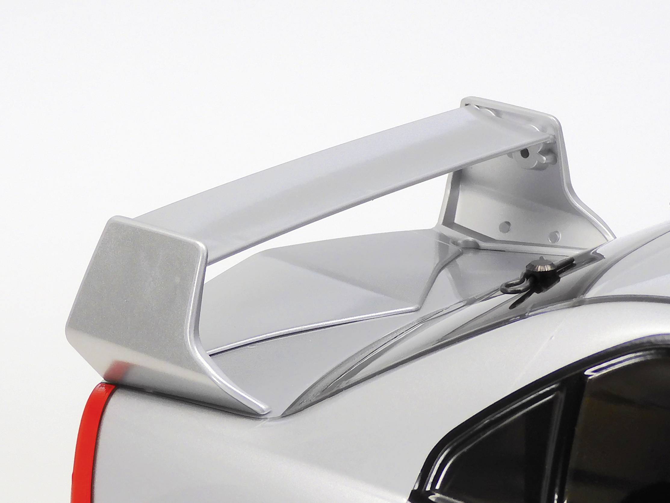 Une voiture de sport argentée avec un grand aileron arrière. L'image se concentre sur la partie arrière aérodynamique du véhicule.