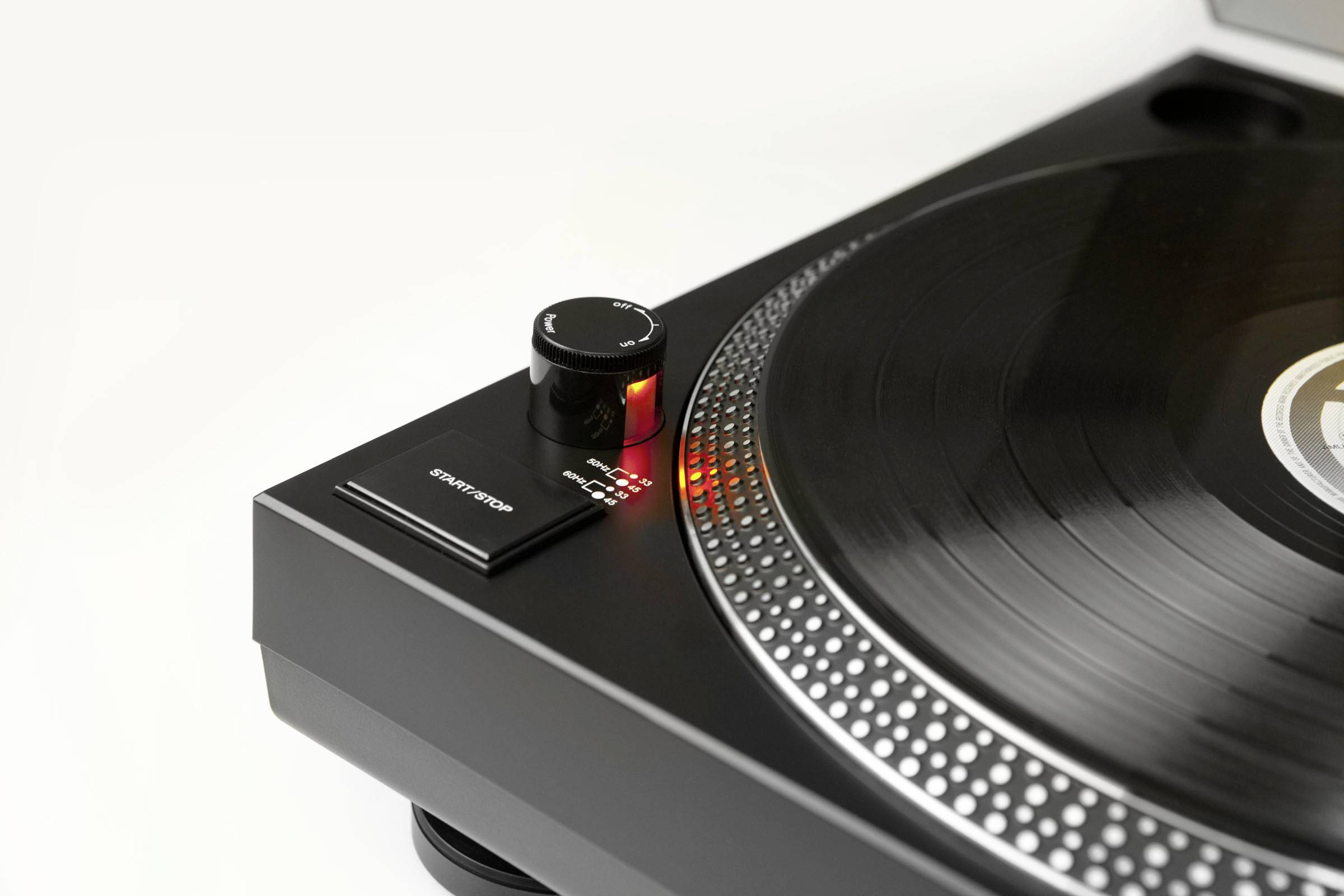 Tourne-disque avec un disque vinyle noir sur le plateau. Un gros plan montre le sélecteur de vitesse avec une LED illuminée.