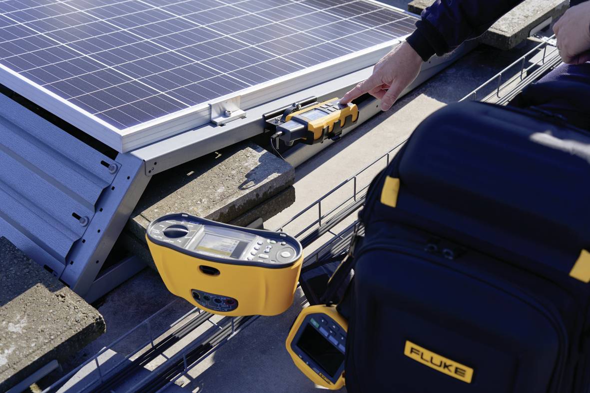 Une personne effectue des mesures sur une installation solaire, avec un appareil de test jaune à proximité d'un module solaire sur un toit.