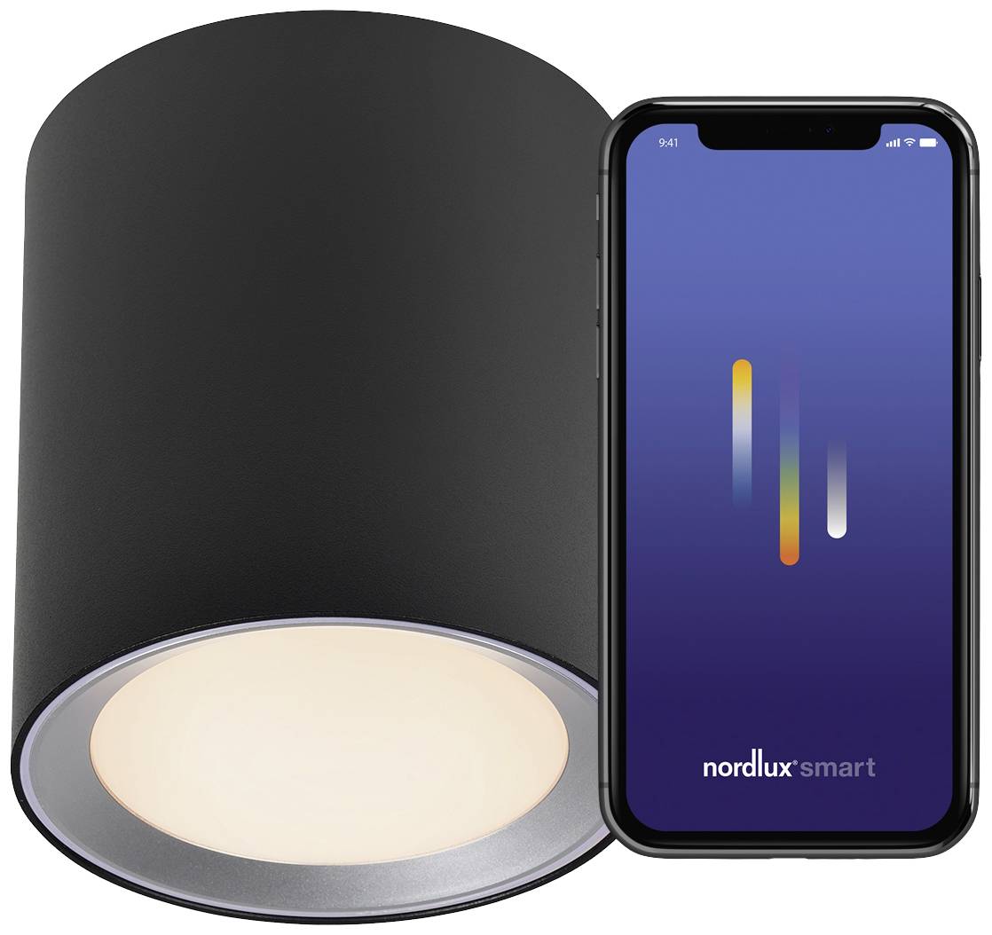 Projecteur de plafond noir à côté d'un smartphone. L'écran affiche l'application 'nordlux smart' avec des éléments de commande colorés pour le contrôle de l'éclairage.