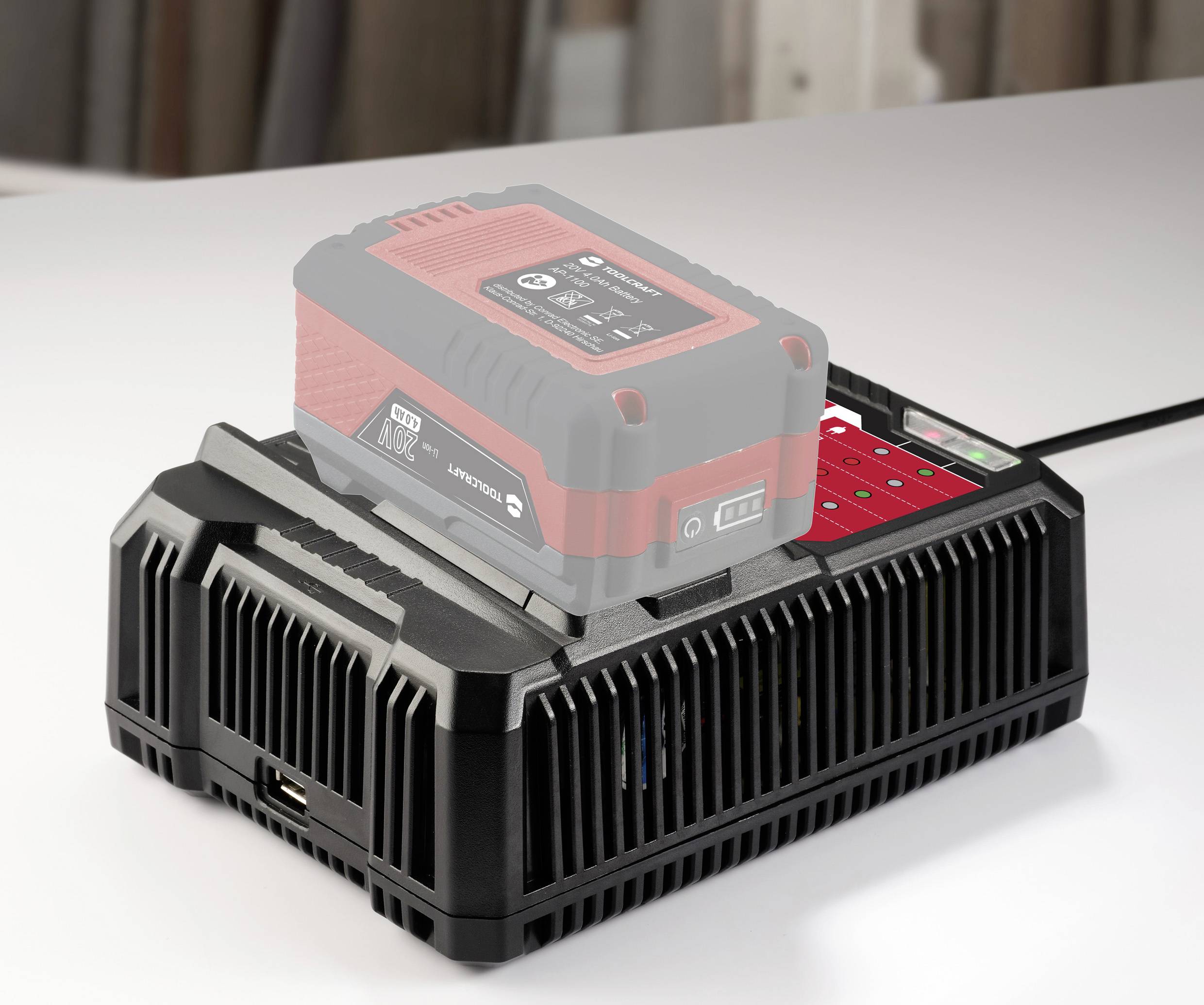 Une batterie rouge est en train de charger sur une station de charge noire. La station de charge affiche un indicateur de charge avec plusieurs points lumineux rouges.
