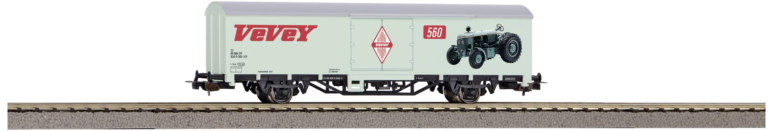 Un wagon de marchandises de train miniature portant l'inscription 'VEBEX' et une image de tracteur sur le côté. Le wagon est posé sur un tronçon de voie ferrée.