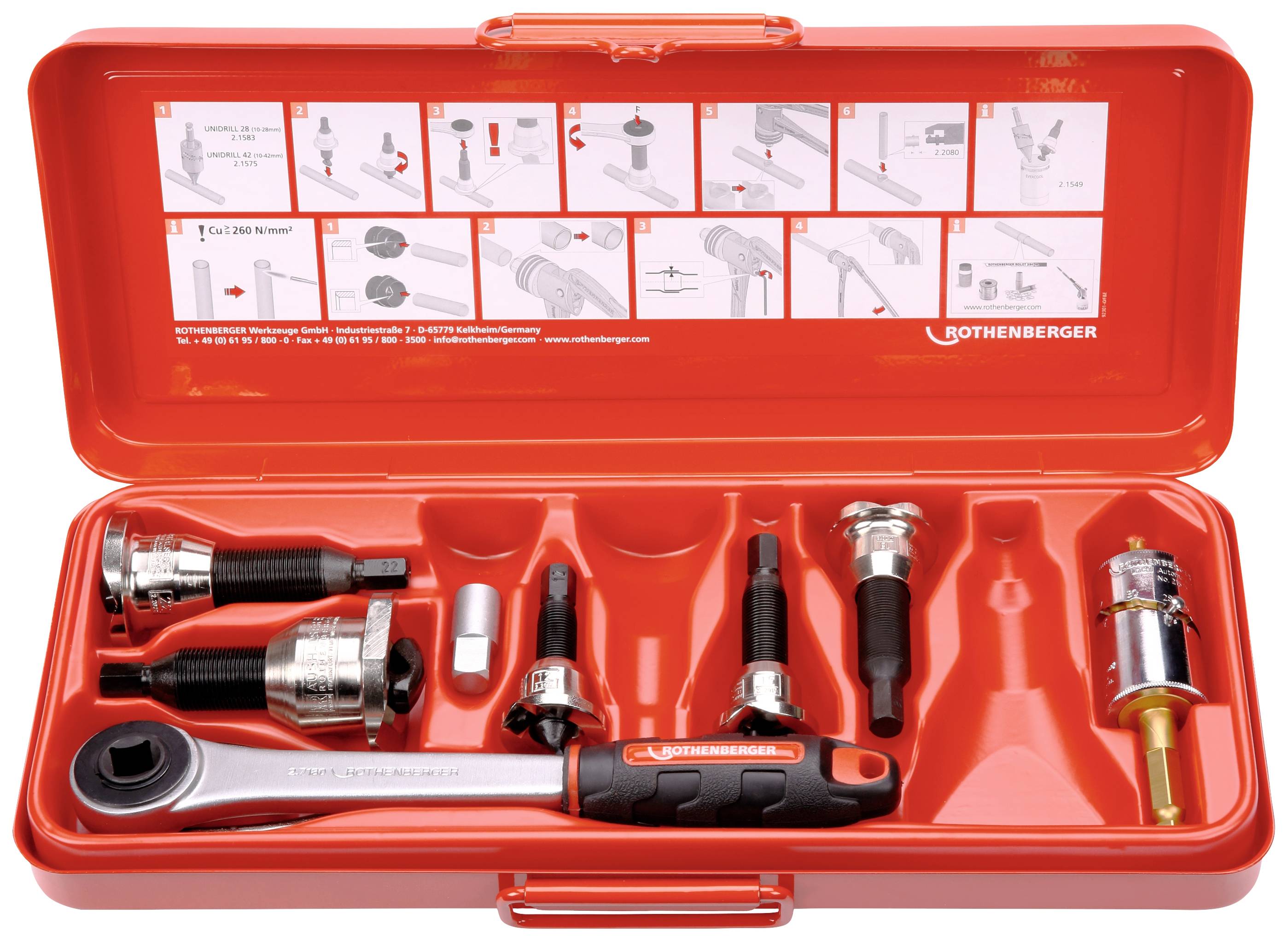 Boîte à outils rouge contenant plusieurs outils, dont une clé à molette, des pinces et des buses, posée sur un support rouge. Diagramme d'instructions sur le couvercle.