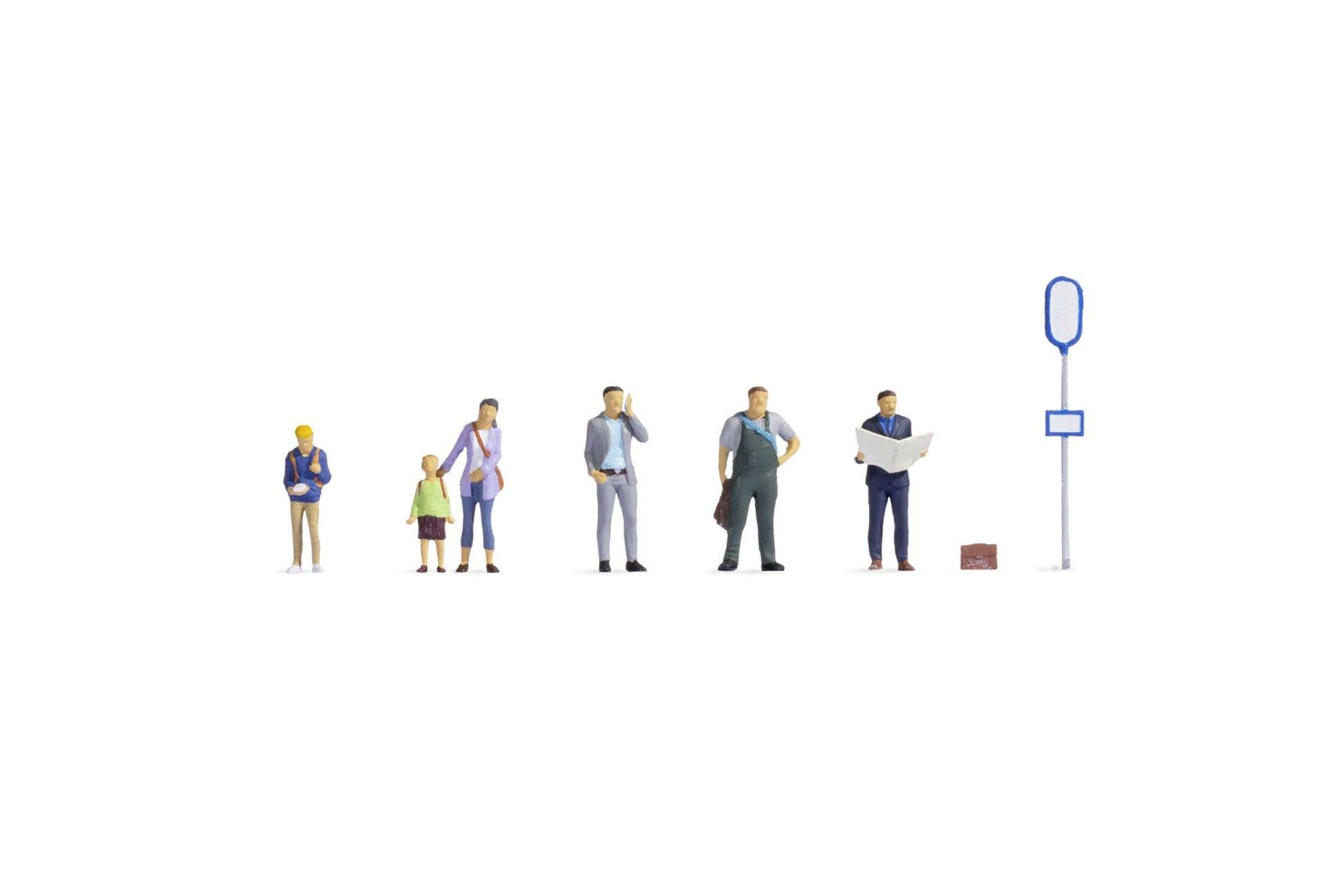 Un groupe de petites figurines se tient à un arrêt de bus. Des hommes et des femmes attendent, une personne tient un journal.