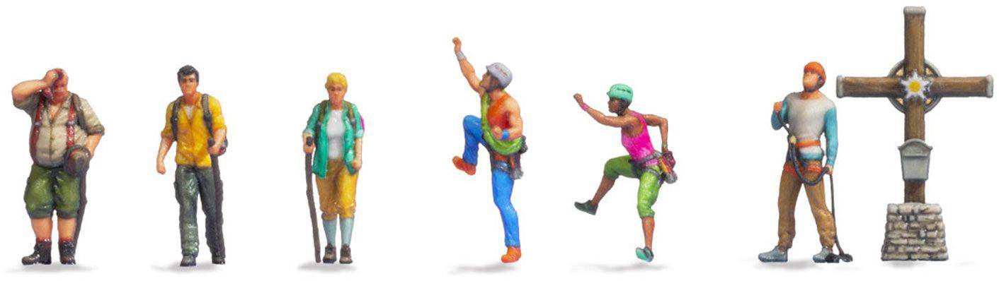 Six figurines miniatures en randonnée, avec différentes poses et équipements. À droite, une croix en bois est dressée sur un socle en pierre.