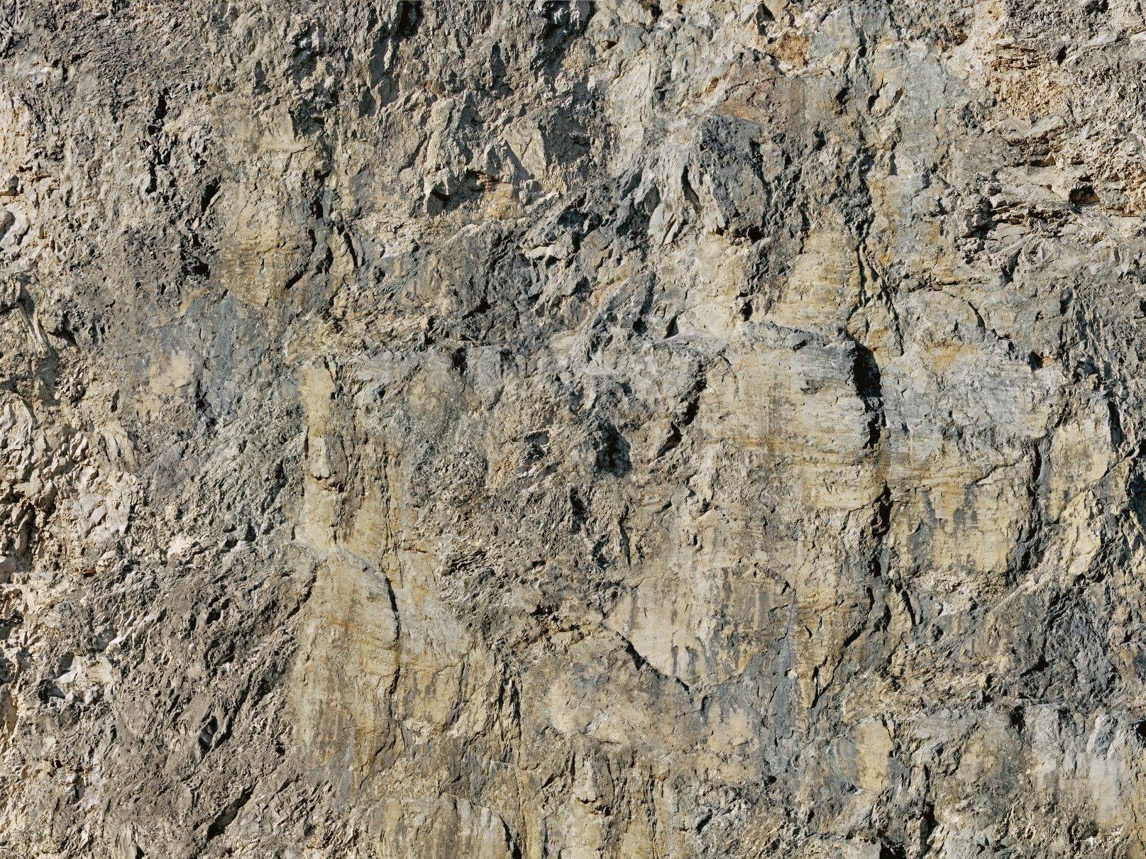 Mur de pierre à structure grossière avec des nuances de gris clair et de beige, révélant des formations rocheuses et des textures naturelles.