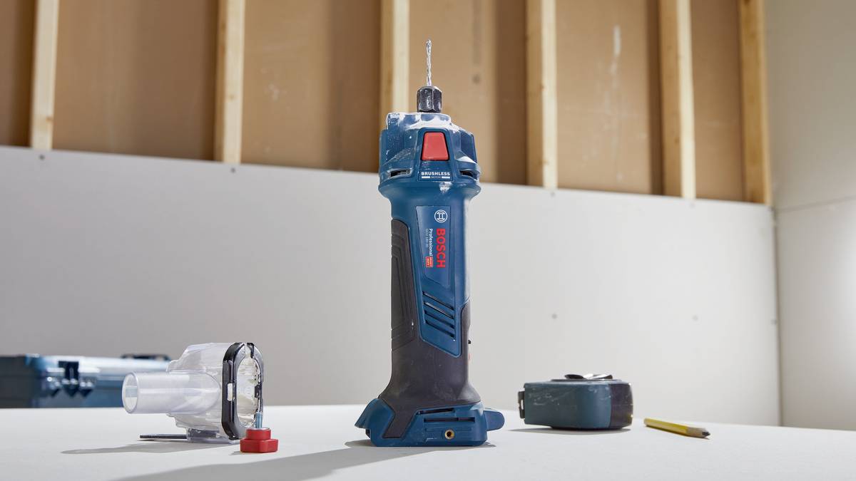 Un outil électrique bleu est posé sur une table, entouré d'une housse en plastique, d'un mètre ruban et d'un stylo ; intérieur d'un chantier de construction.