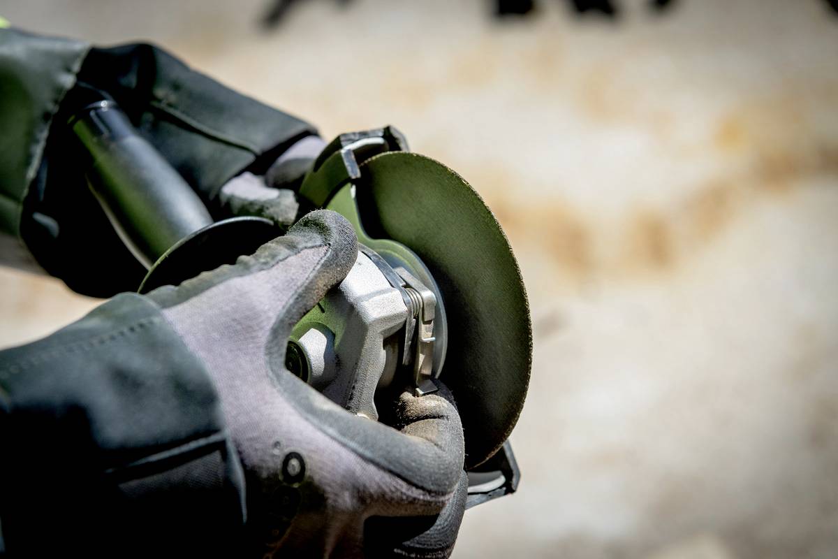 Gros plan sur des mains portant des gants de protection, tenant une meuleuse rotative. Des étincelles volent lors de l'usinage du métal.