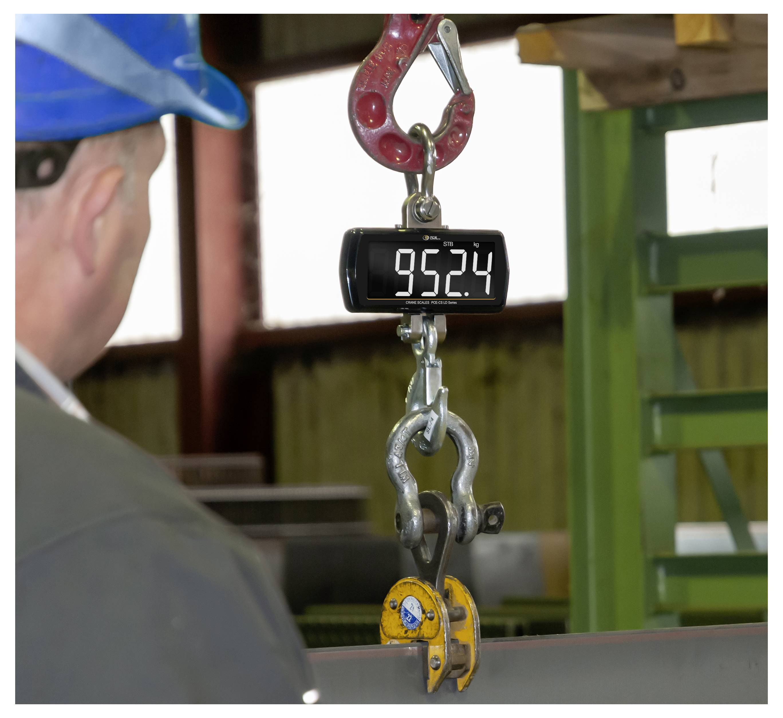 Balance numérique suspendue affichant 952,4 kilogrammes en suspension à un crochet de grue dans un environnement industriel.