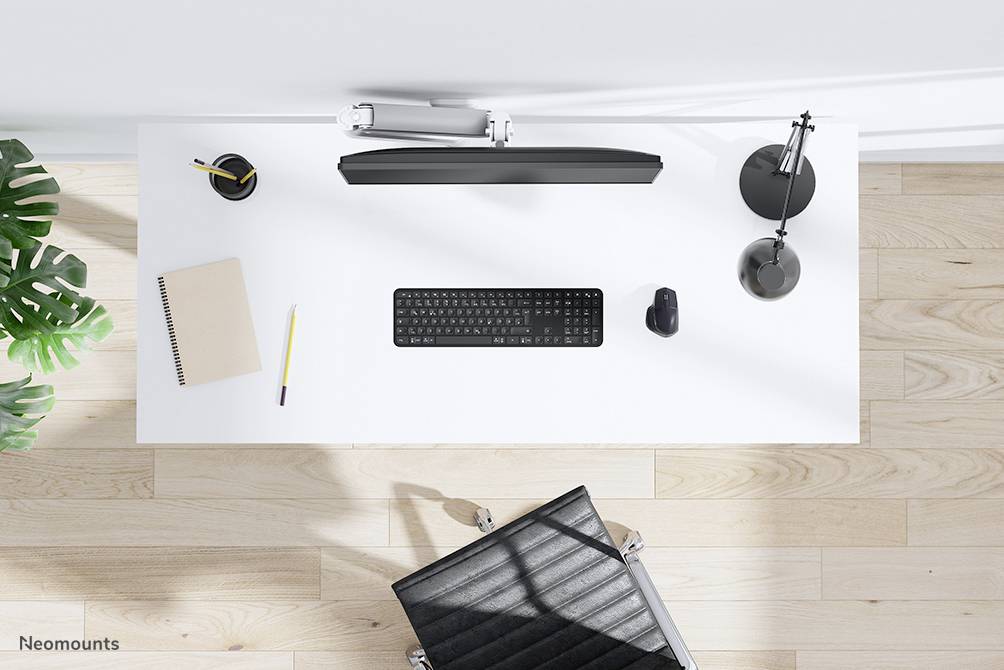 Un bureau moderne et minimaliste vu de dessus : clavier, souris, lampe, stylo, carnet et plante sur un sol en bois clair.