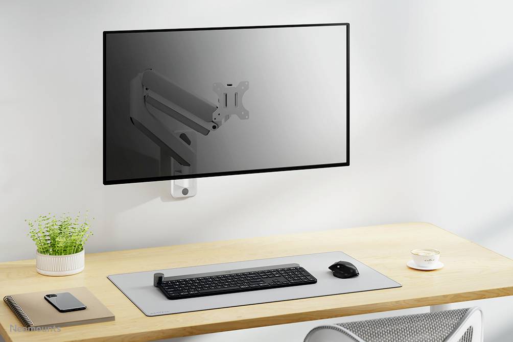 Support de moniteur plat fixé au mur, au-dessus d'un bureau minimaliste équipé d'un clavier, d'une souris, d'un carnet, d'une plante et d'une tasse.