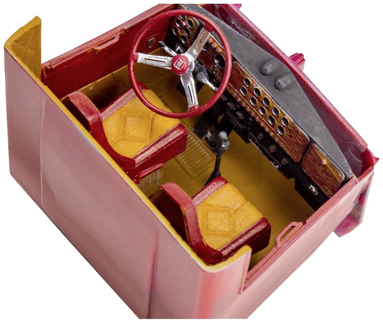 Intérieur d'une voiture miniature rouge avec volant et deux sièges jaunes. Tableau de bord détaillé avec de nombreux boutons et interrupteurs.