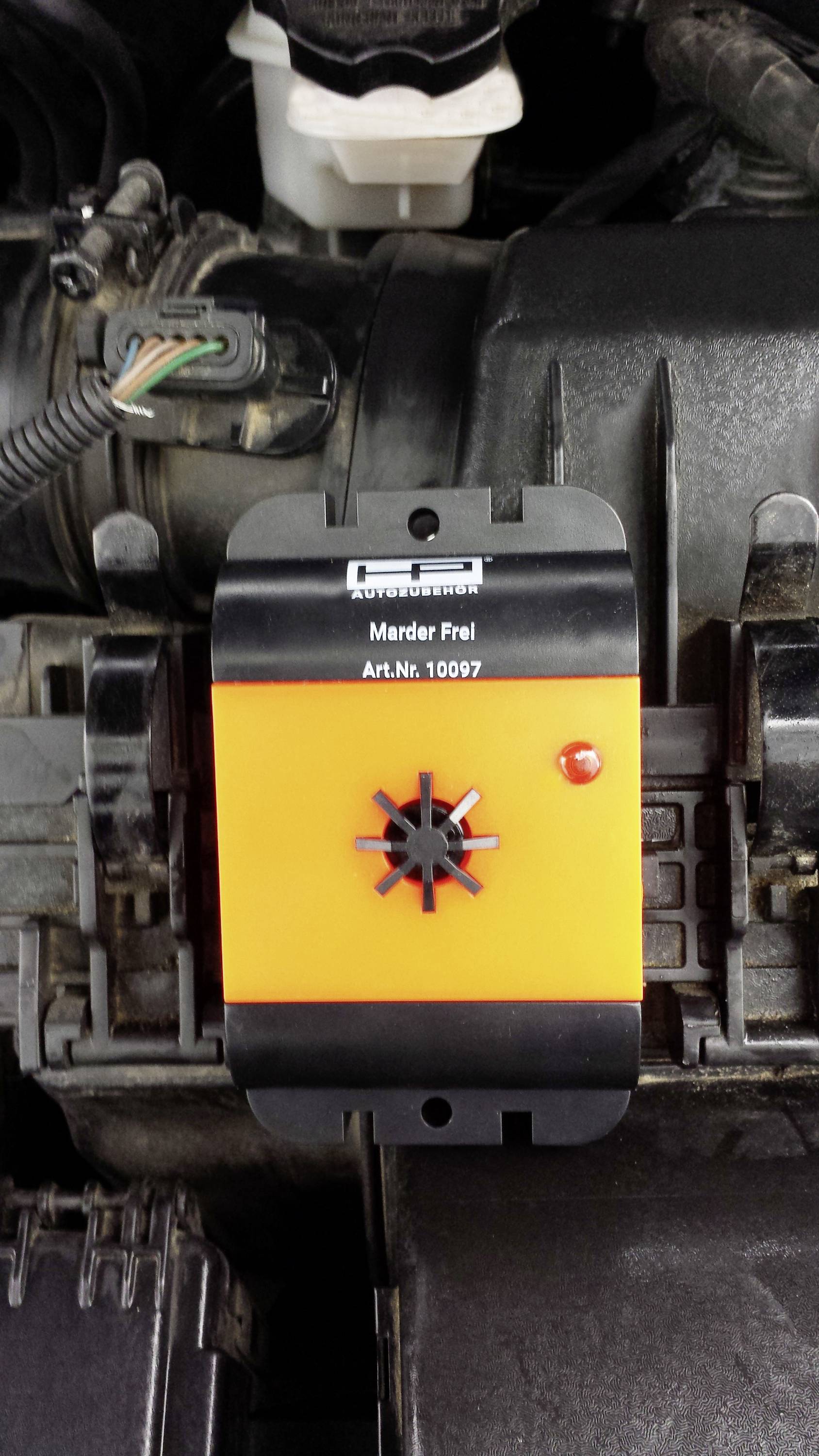 Répulsif anti-fouine orange avec boîtier noir et voyant de contrôle rouge, installé dans un compartiment moteur.