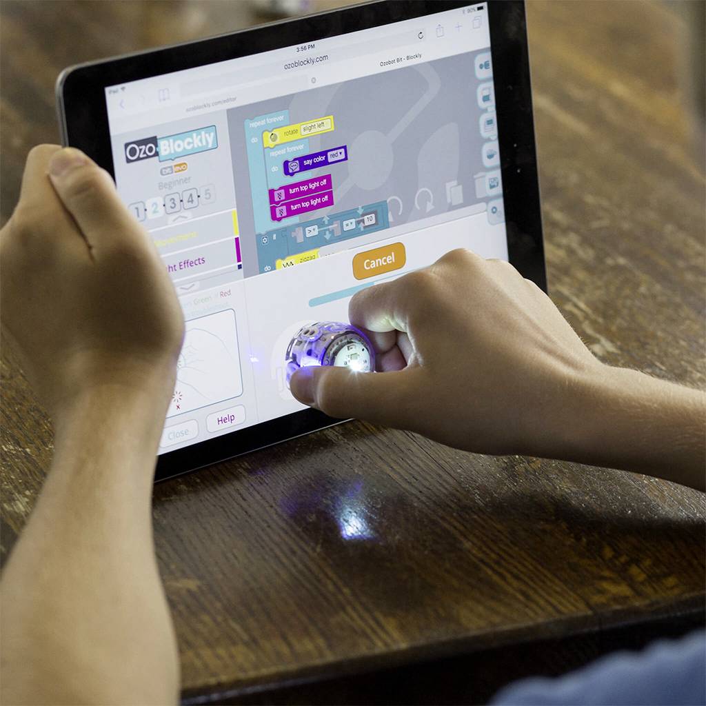 Une personne programme un petit robot à l'aide d'une application sur tablette. Le robot s'illumine et indique qu'il est en marche.