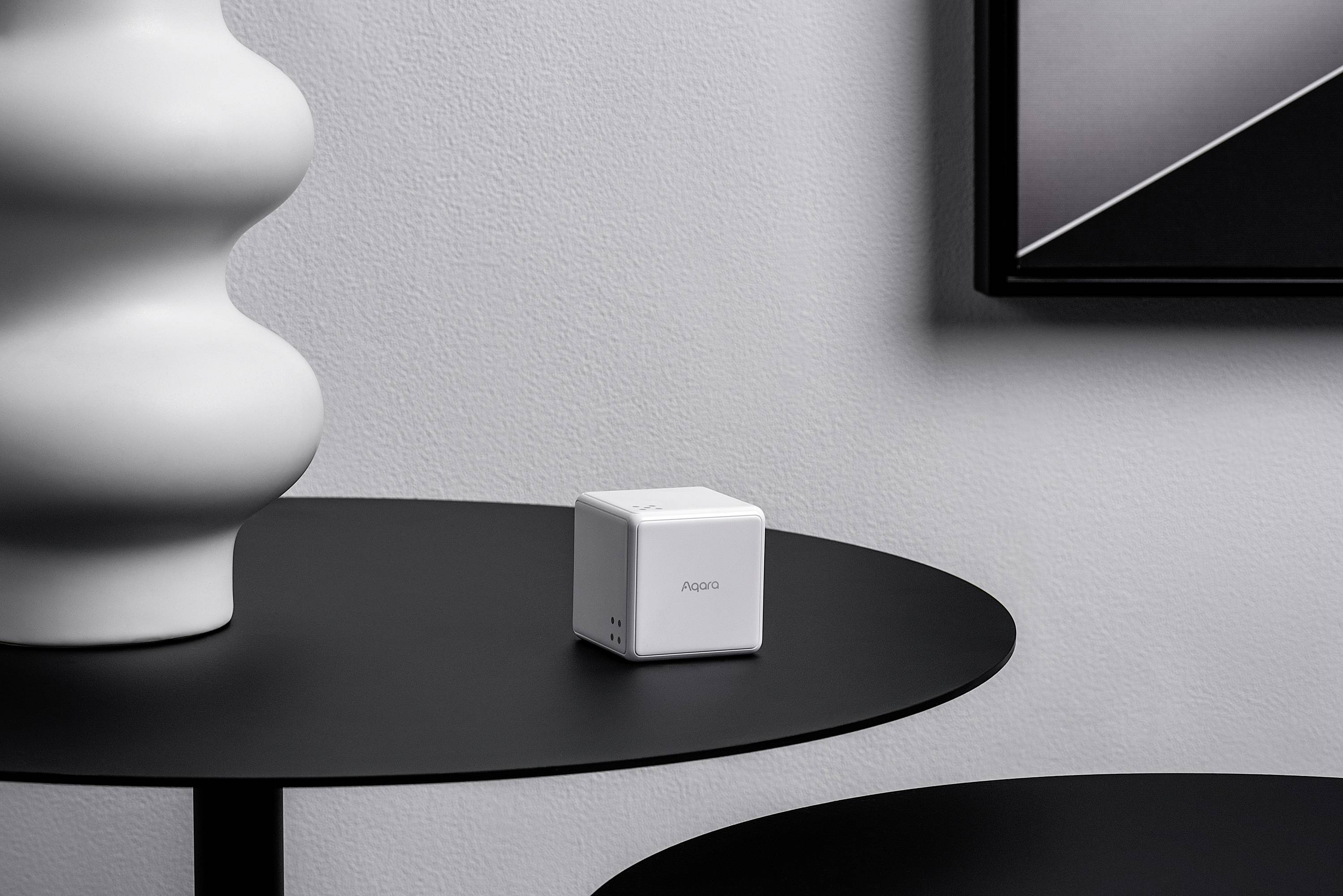 Un cube blanc portant l'inscription 'HD03' est posé sur une table ronde noire dans une pièce minimaliste.