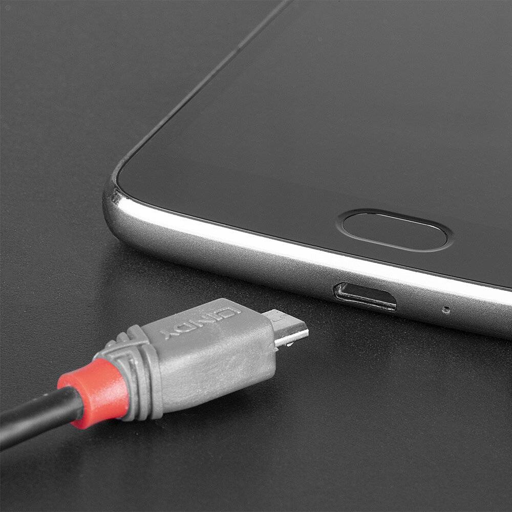 Un smartphone est posé sur une table, à côté duquel se trouve un câble USB. Le câble est prêt à être branché à l'appareil.
