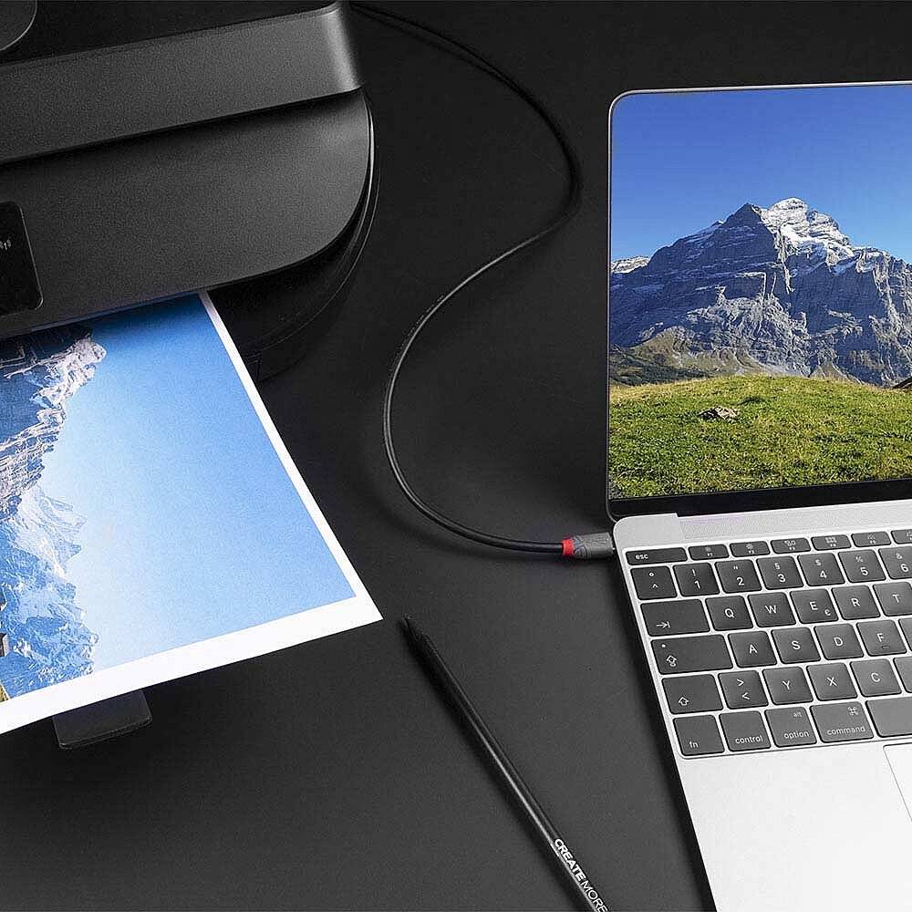 Un ordinateur portable est posé à côté d'une imprimante qui imprime une photo d'un paysage de montagne. Un câble USB relie l'ordinateur portable à l'imprimante.