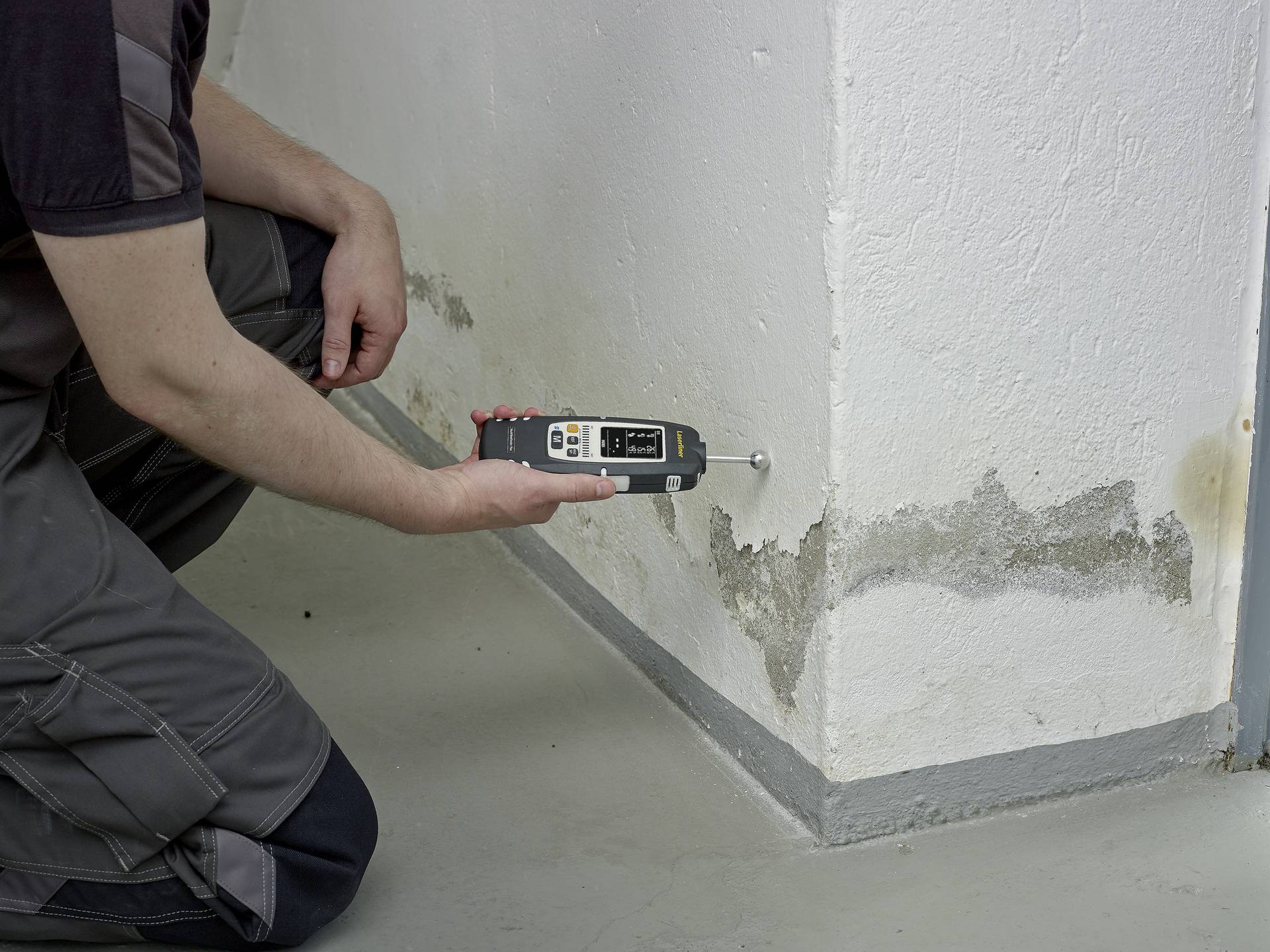 Une personne mesure l'humidité dans un mur affecté par des taches d'eau et des dommages potentiels de moisissure à l'aide d'un appareil.