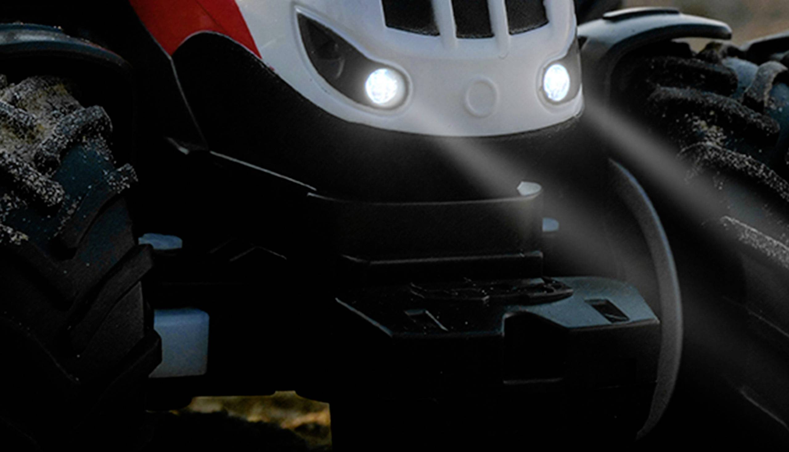 Un tracteur jouet avec des phares avant lumineux sur un fond sombre ; de grandes roues montrant des détails pour des trajets tout-terrain.