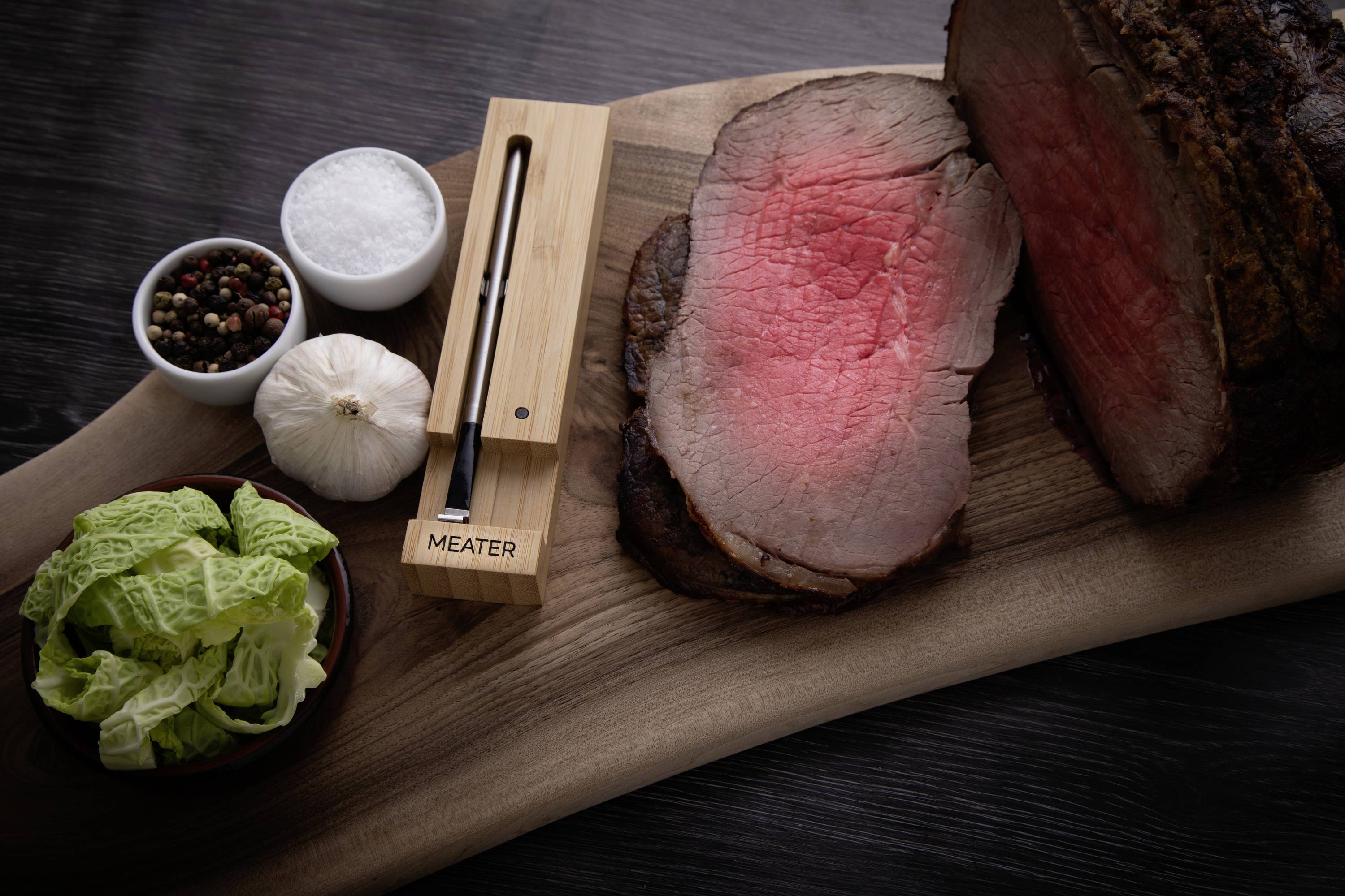 'Tranche d'un rosbif moyennement cuit sur une planche en bois, décorée de sel, de poivre, d'ail, de salade et d'un thermomètre à viande.'
