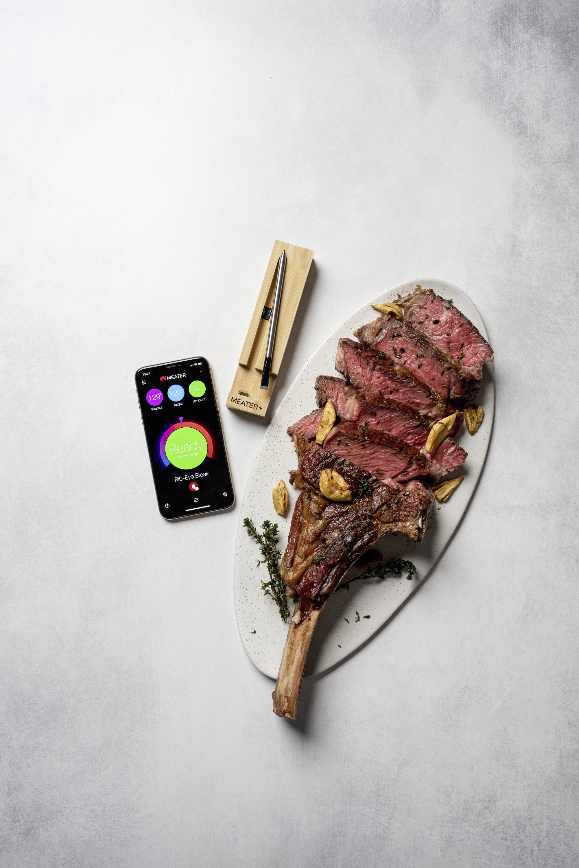 Un steak tranché sur une assiette ovale, accompagné d'un smartphone affichant une application et d'un thermomètre à viande.