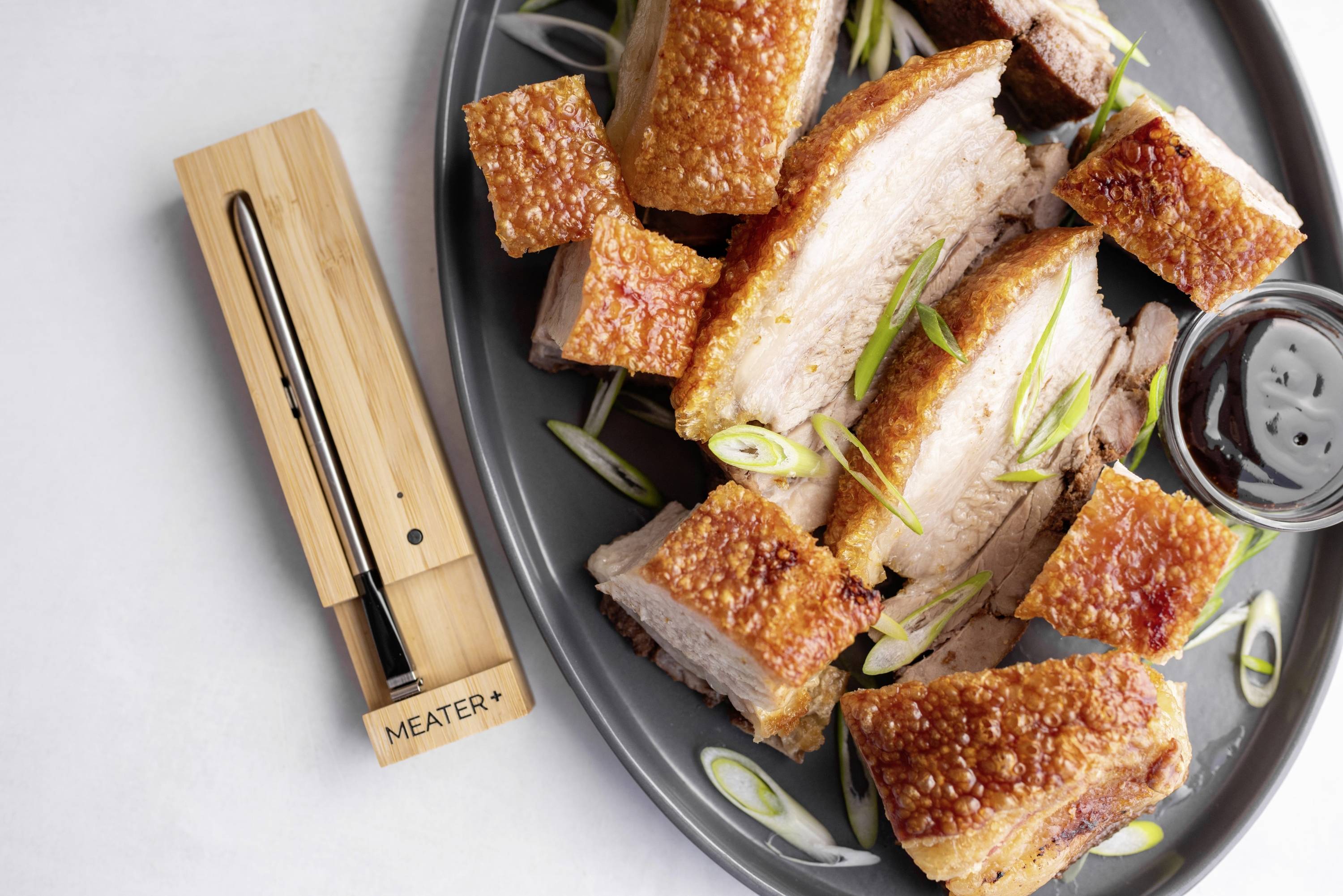 Rôti de porc à croûte croustillante dans une assiette, décoré de ciboulette. À côté, un thermomètre de cuisson numérique.