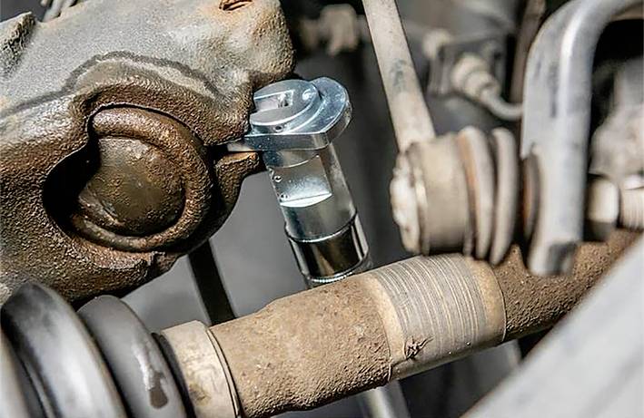 Gros plan de pièces automobiles dans le moteur d'un véhicule. On y distingue un arbre de transmission et d'autres composants mécaniques dans un état de corrosion.